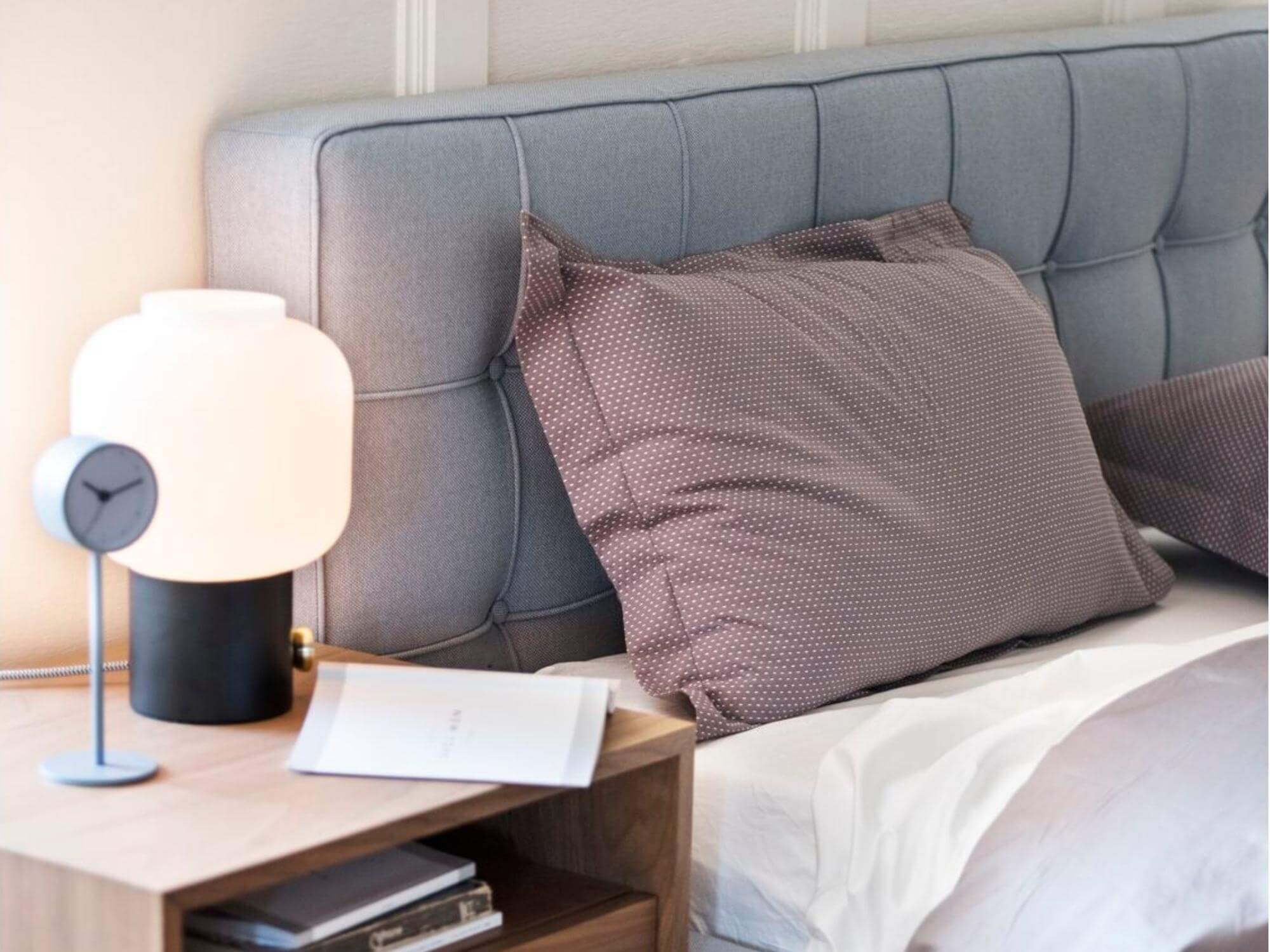 Blue upholstered bed beside mid century walnut nightstand