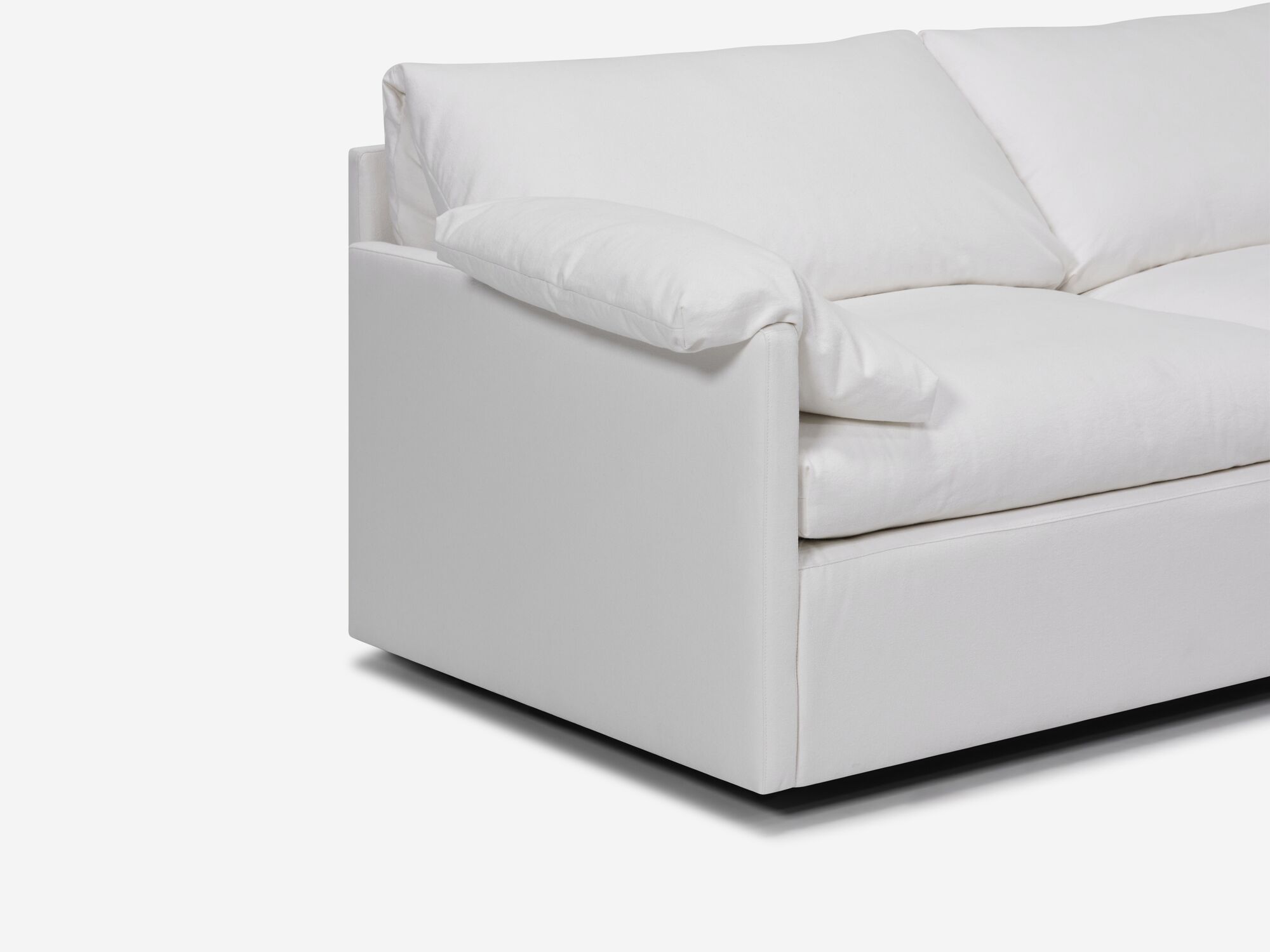Detail view of white sectional sofa with narrow arms, pillow and right hand chaise