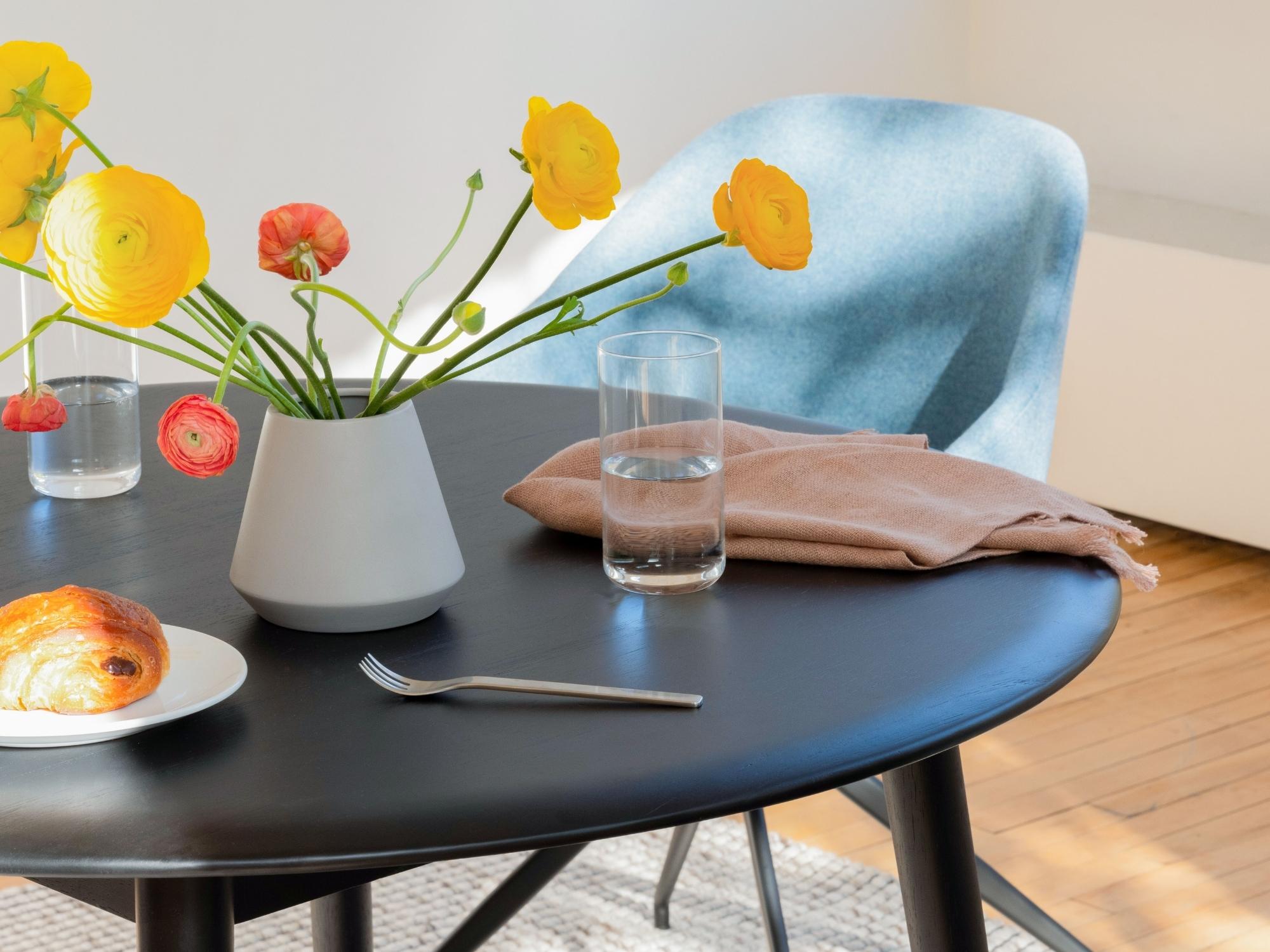 Highball glass, flower vase, and pink napkin on wood dinette table