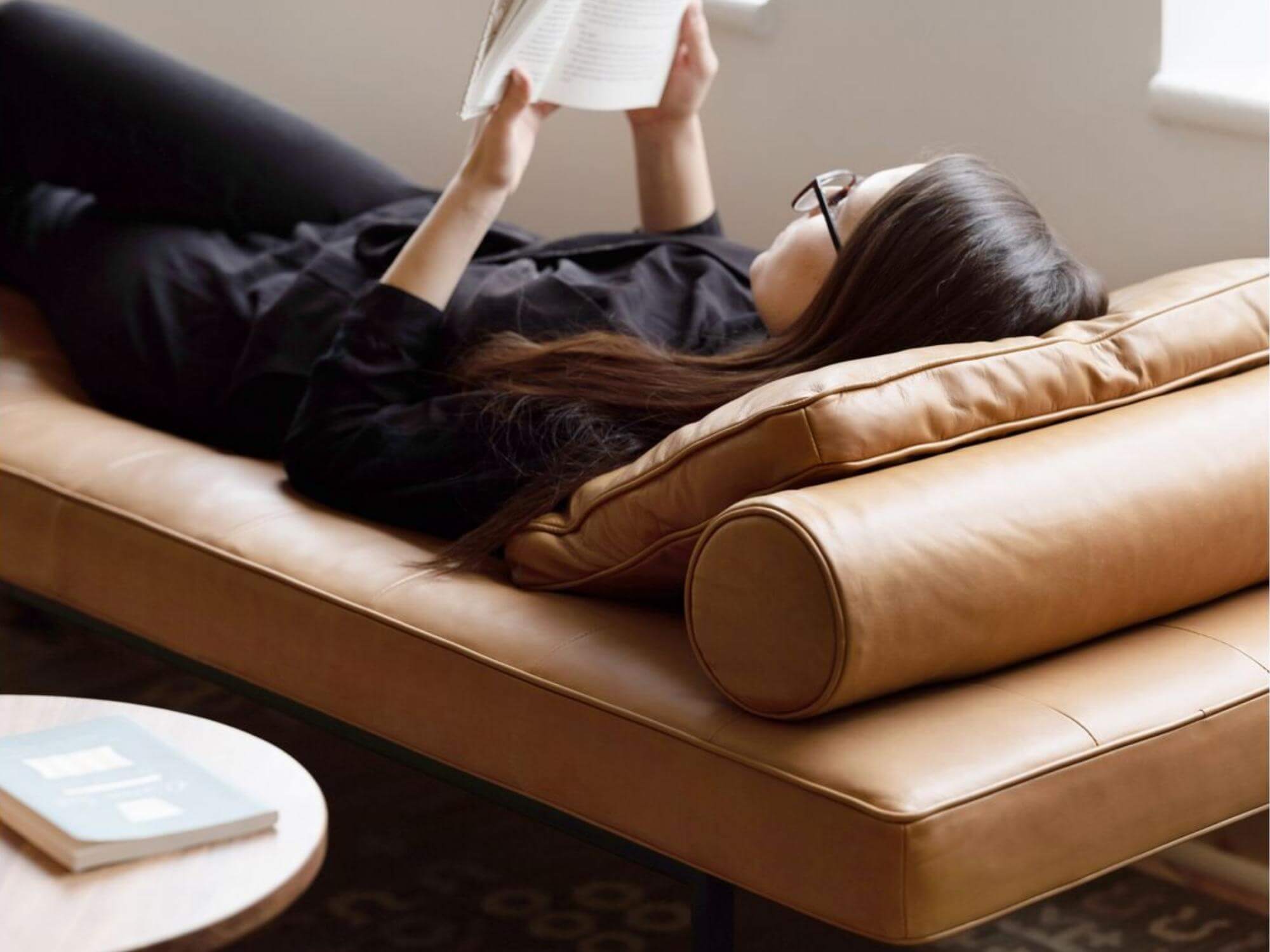 Woman reads on leather chaise with brown leather square pillow