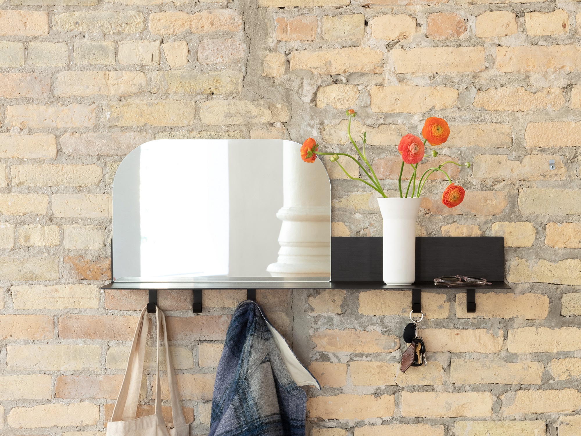 Black metal entryway shelf with hooks and mirror attached to exposed brick wall