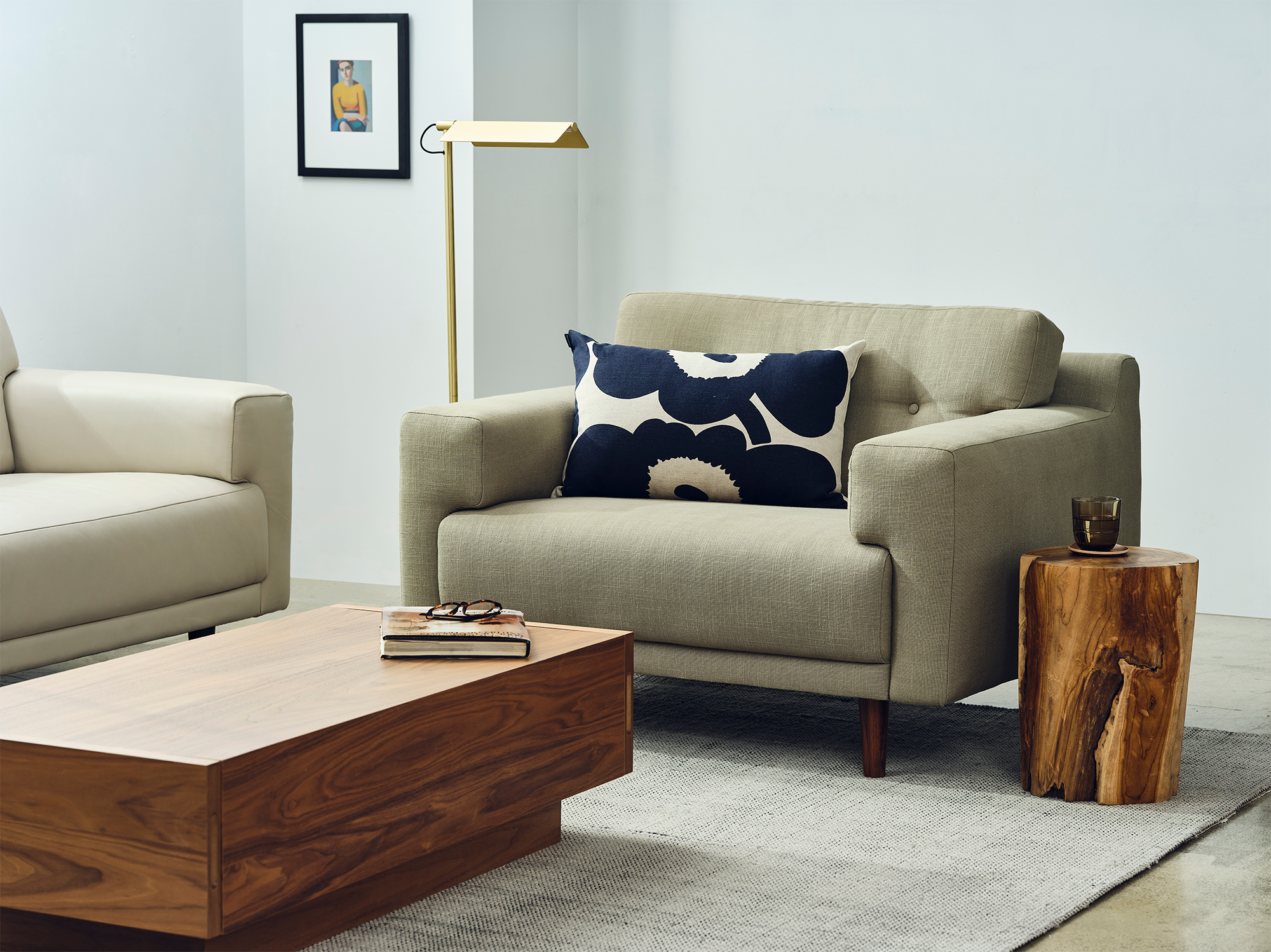 A teak wood stool acts as an end table beside a grey armchair with a walnut coffee table