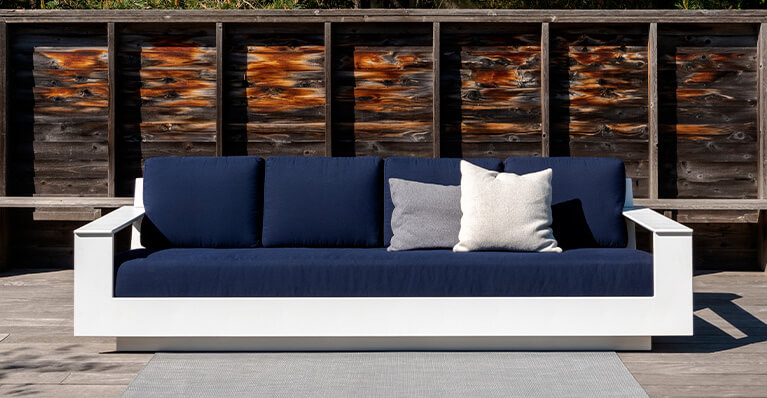 Blue and white outdoor sofa is shown in a cement patio. Link to loll sale page