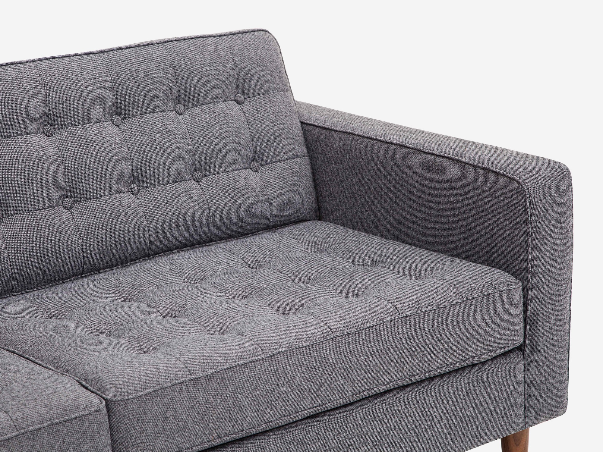 Detail view of grey tufted apartment sofa with black ash legs