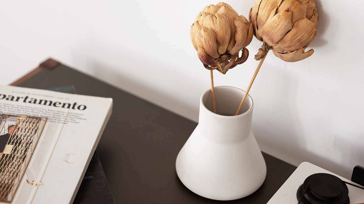 Small white ceramic vase with dried plants in it on black accent table