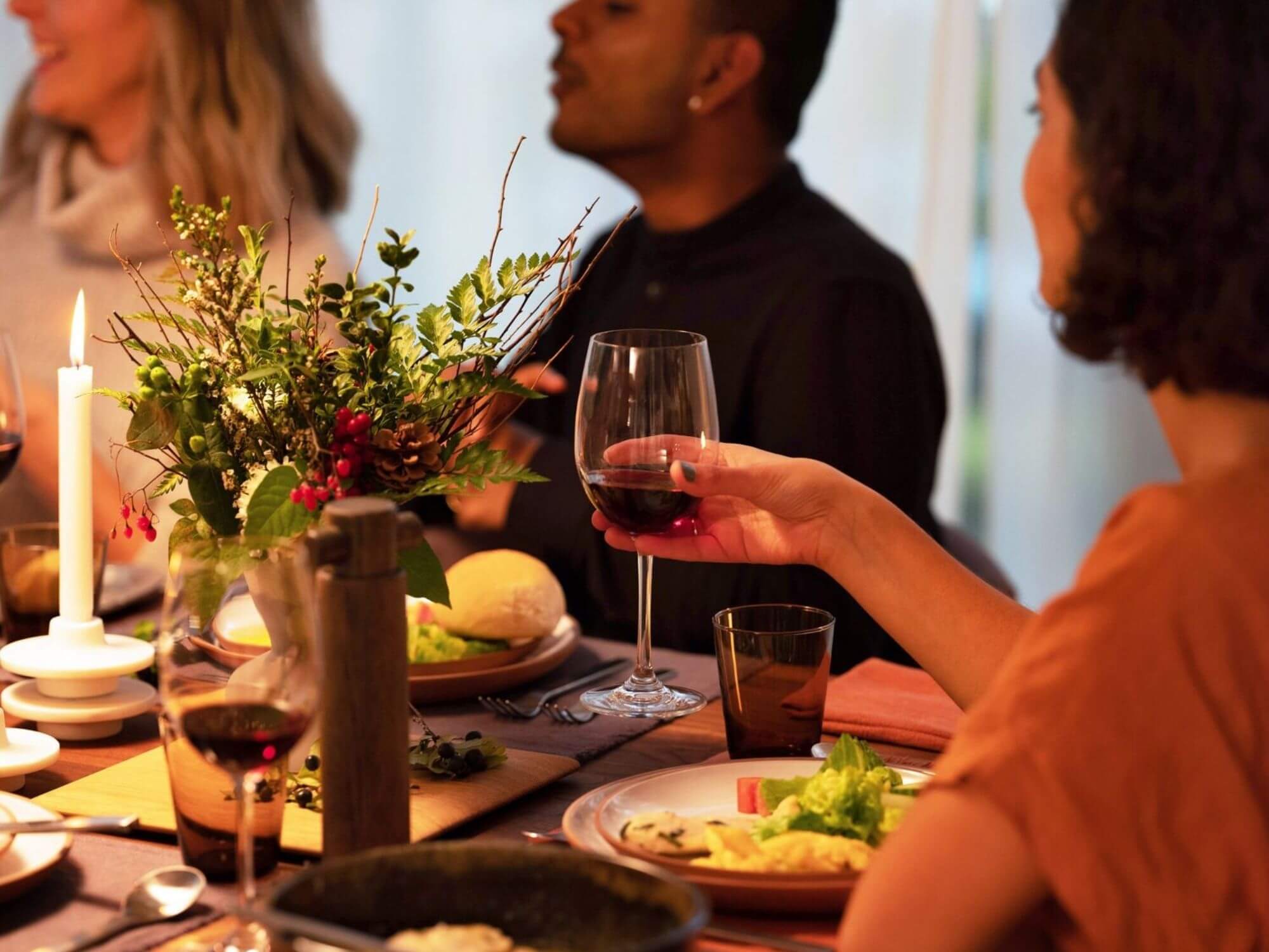 Red wine glass held by a woman sitting at a wood dining table