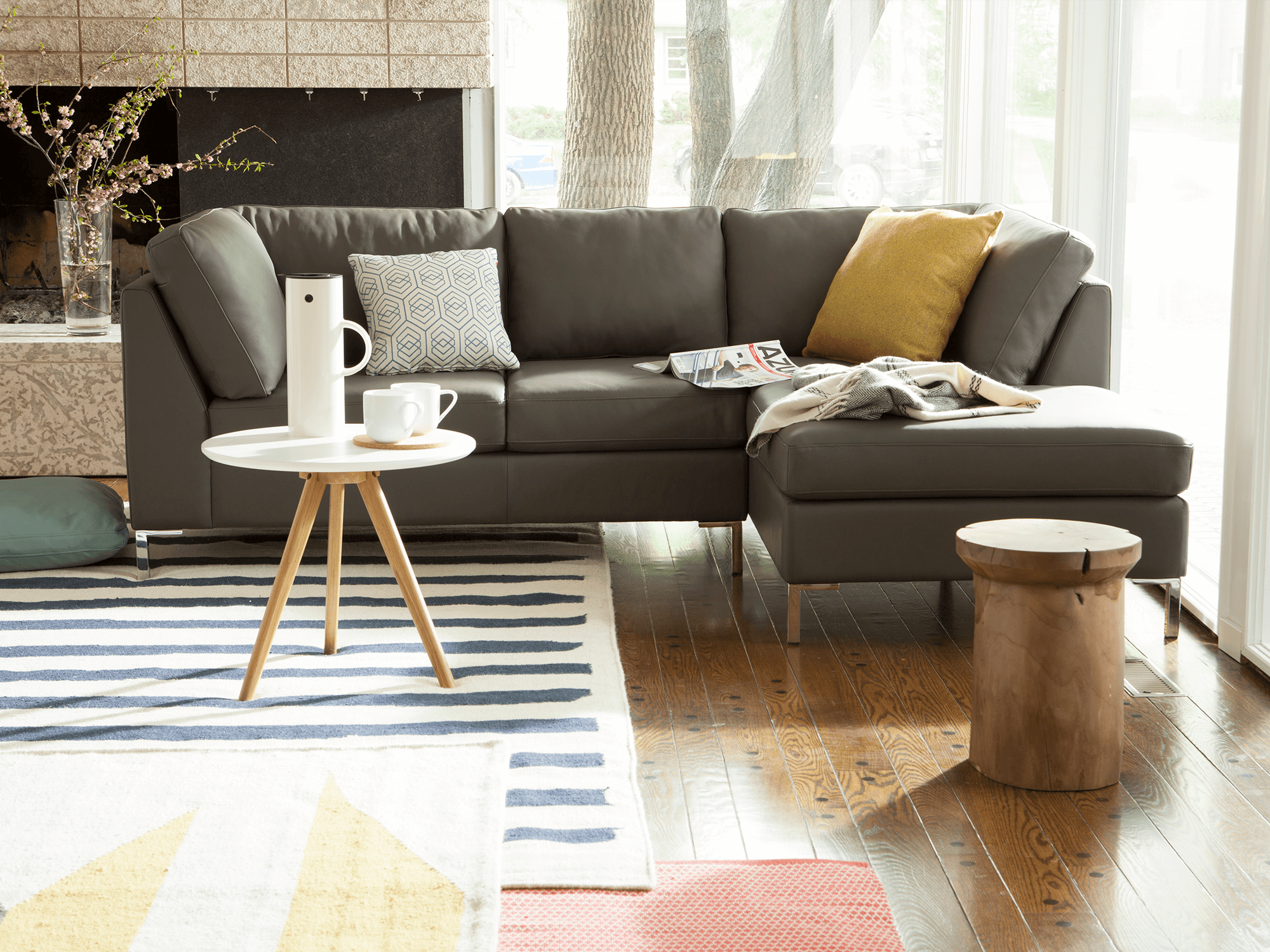 Sustainable teak stool sits beside a gray leather sectional sofa with colorful rugs