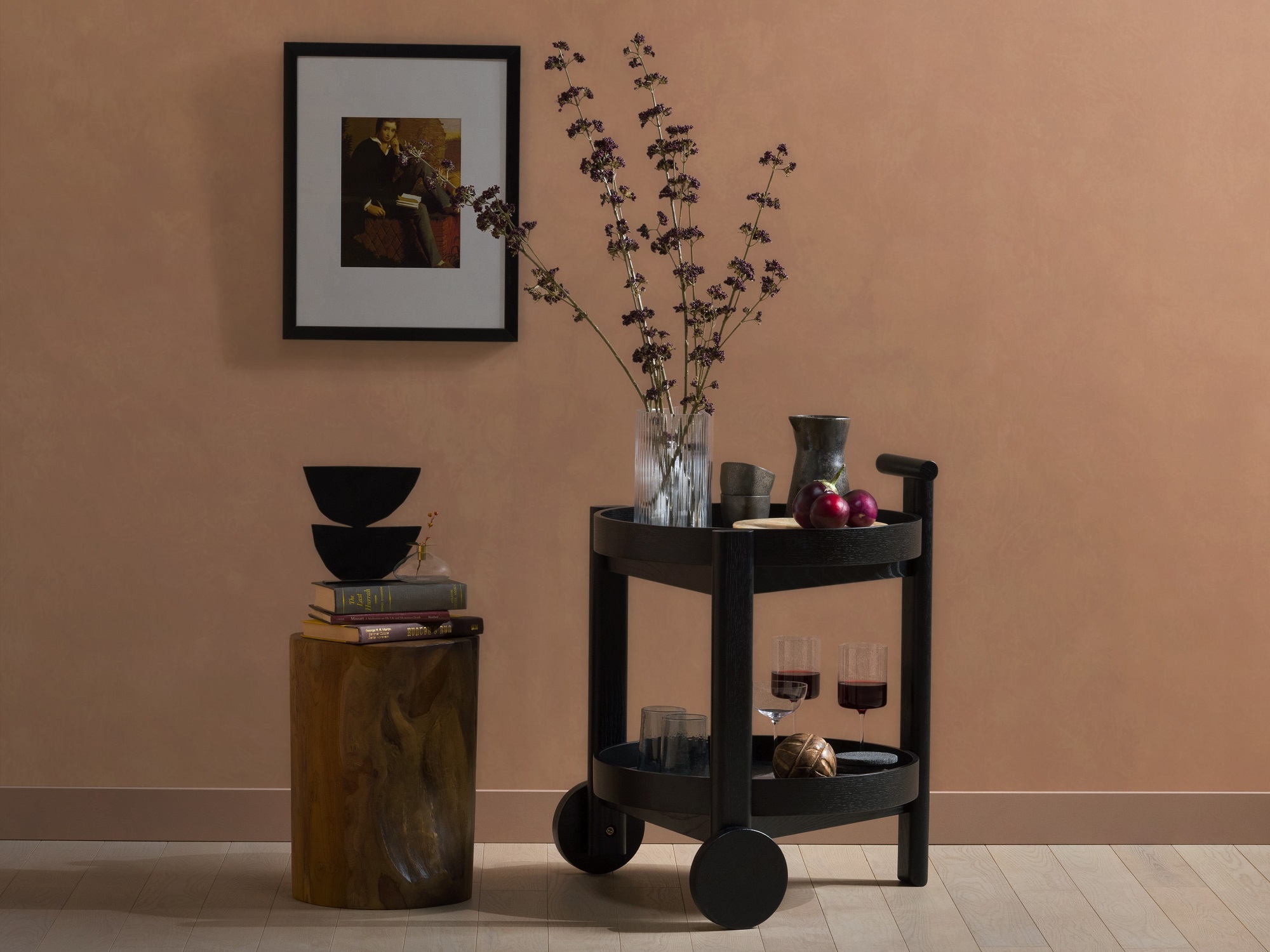 Black oak bar cart with dishes on it beside reclaimed teak stool and framed art