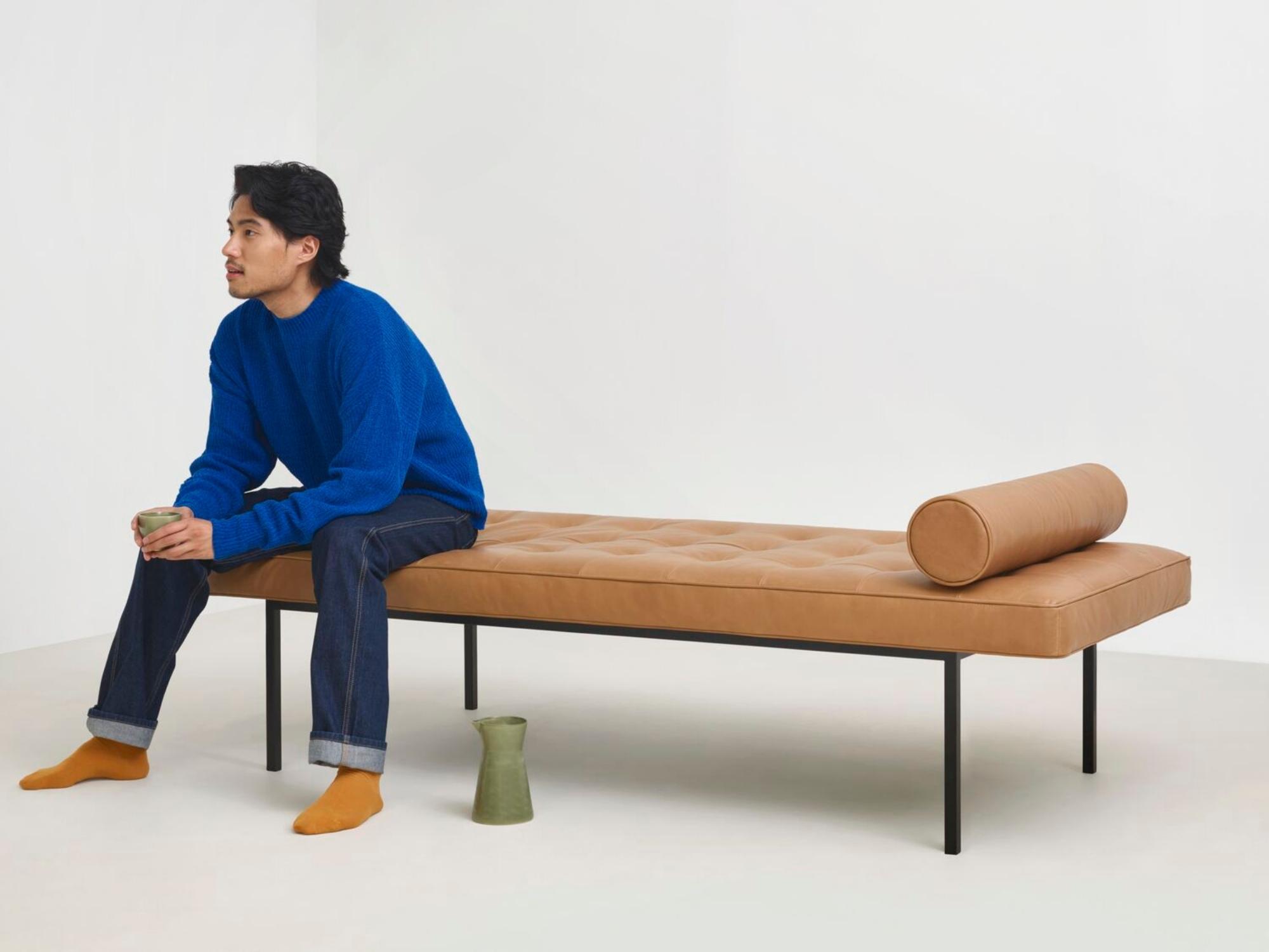 Man sitting on end of brown leather daybed with long round cushion