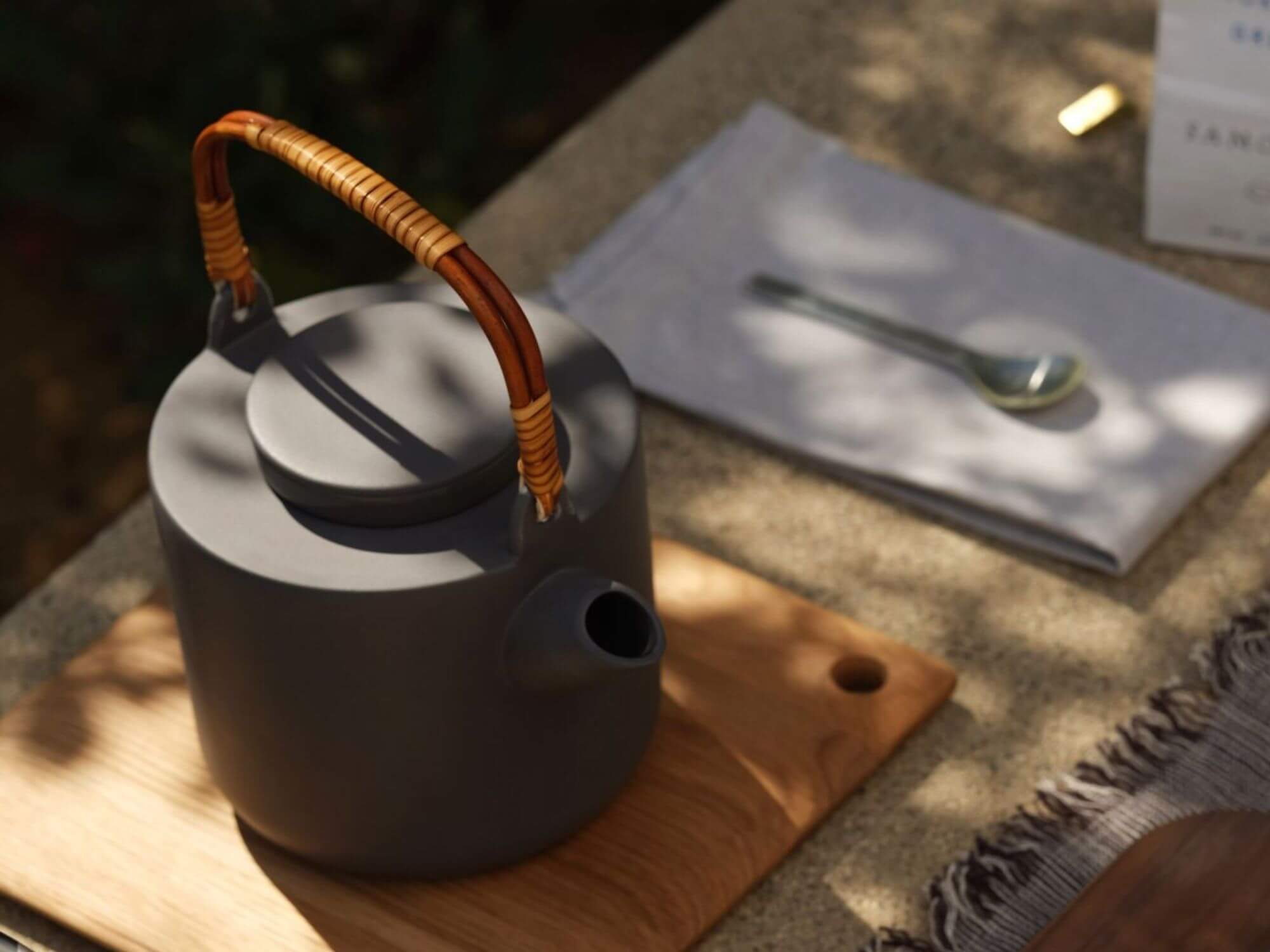 Grey stoneware tea pot sits on a bamboo pot holder outside