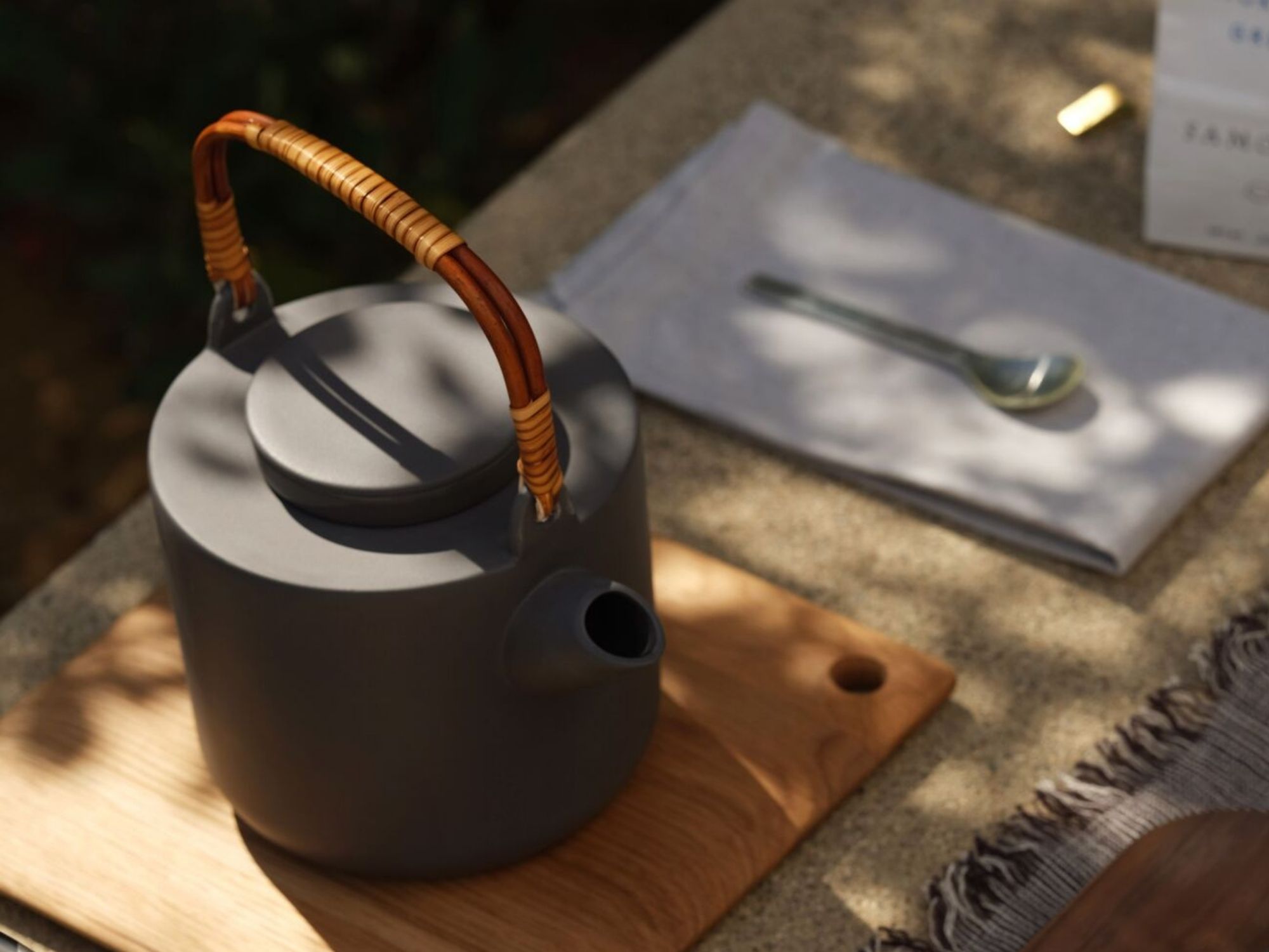 Gray stoneware tea pot sits on a wooden pot holder outside