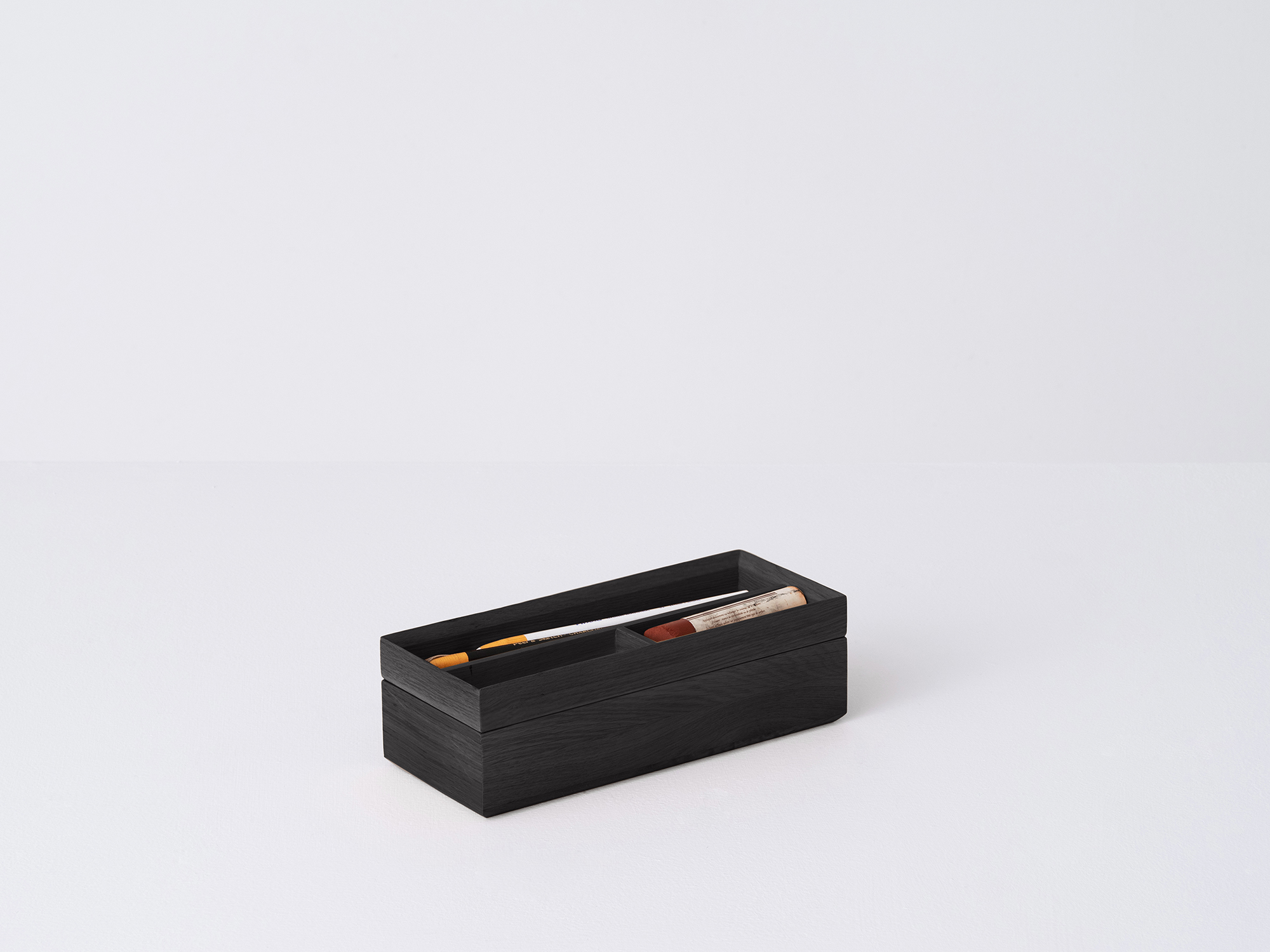 Angled view of the small Draft Pencil Box in black oak with pencils in the top