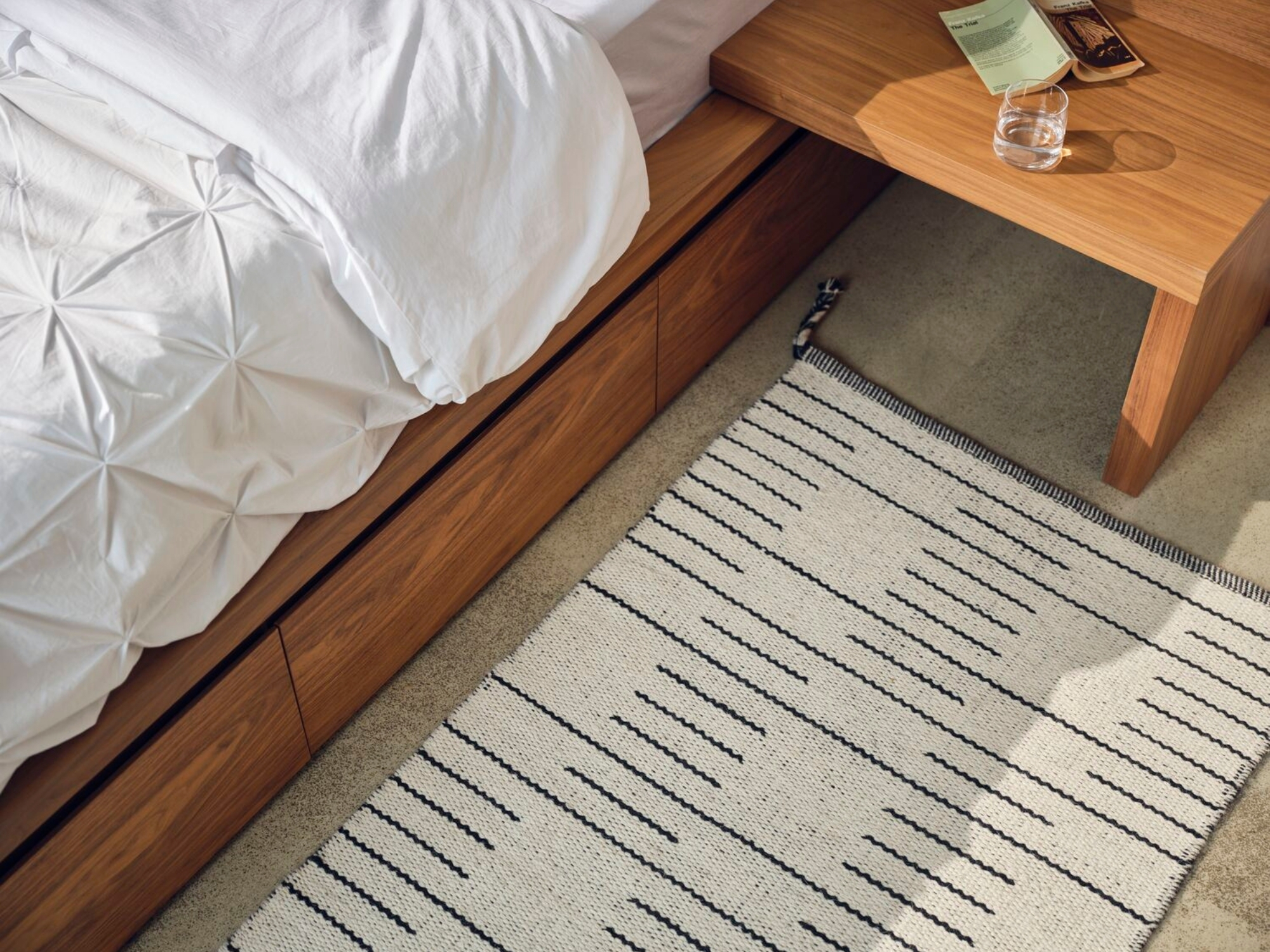 Edge of textured white duvet set on walnut bed