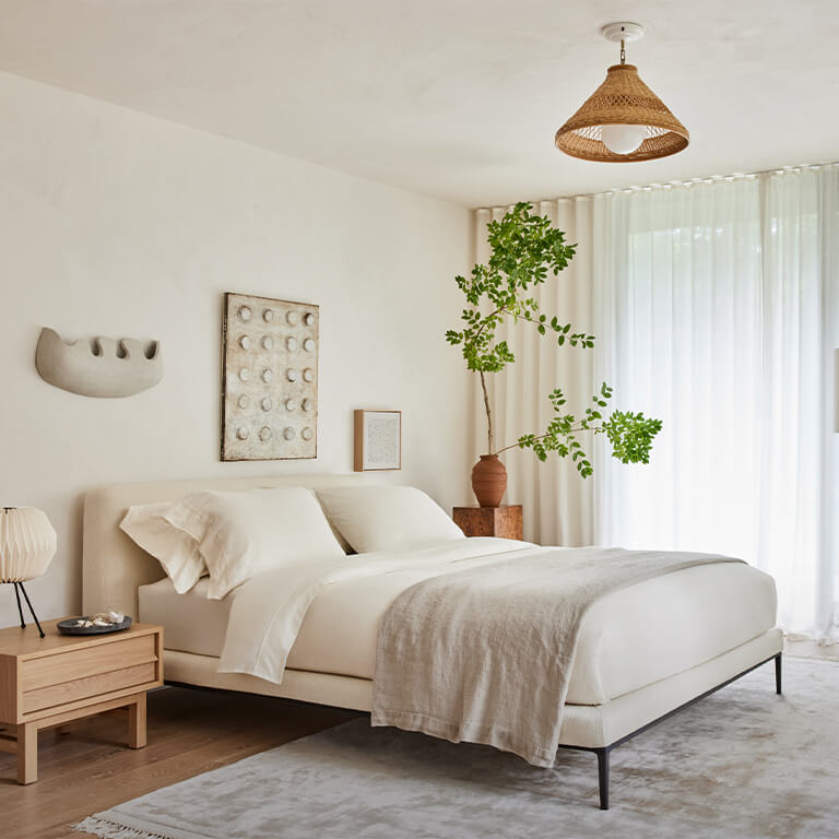 Fabric bed with light color bedding is shown in a bedroom setting