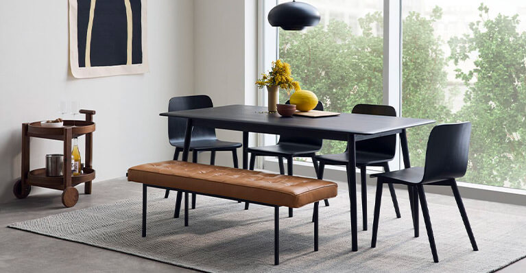 black dining table with matching chairs and leather bench is shown in a dining room setting. Link to dining category