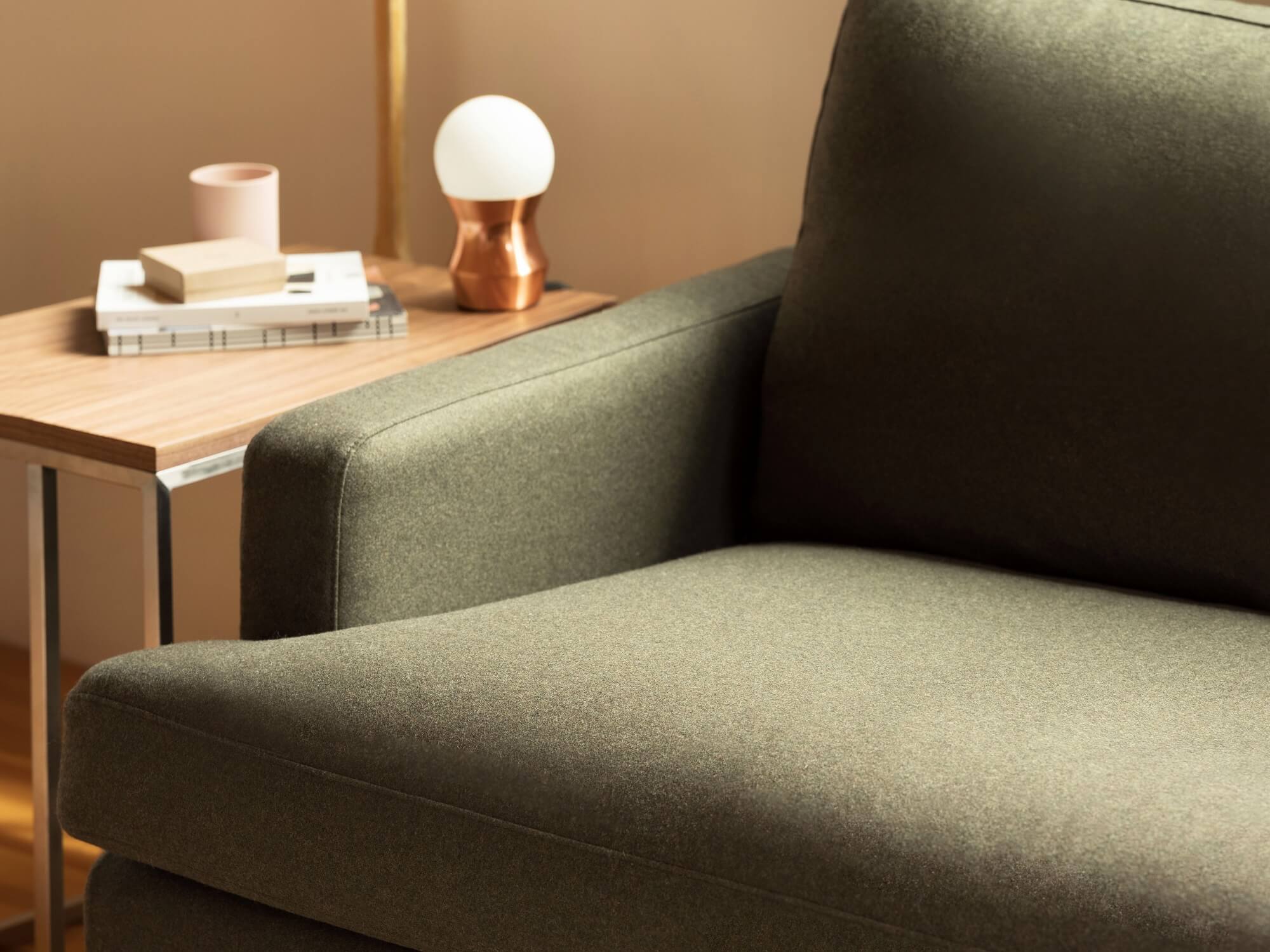 Detail of green sofa arm beside oak end table with lamp on it