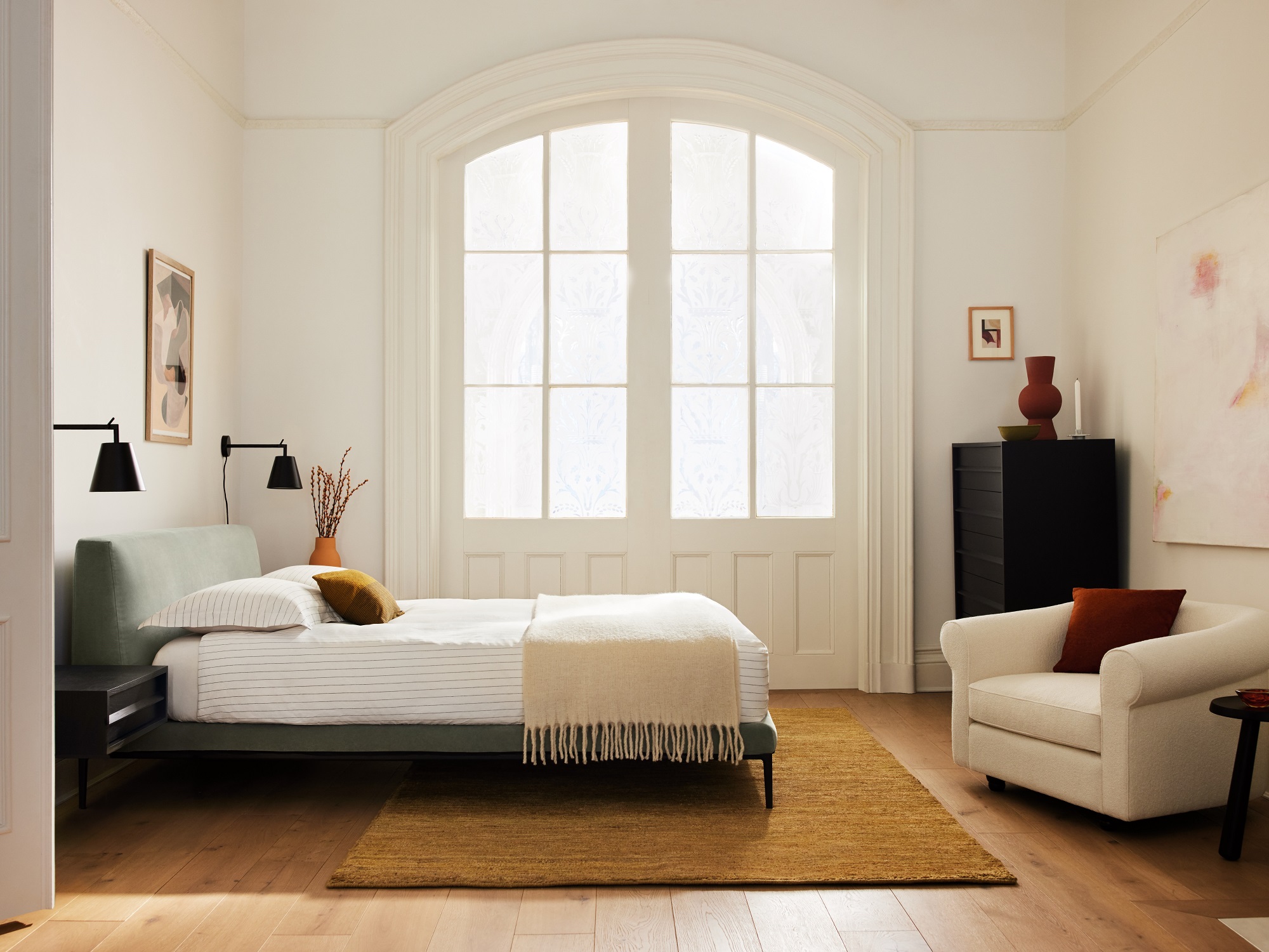 Green upholstered bed frame in bedroom with arched windows