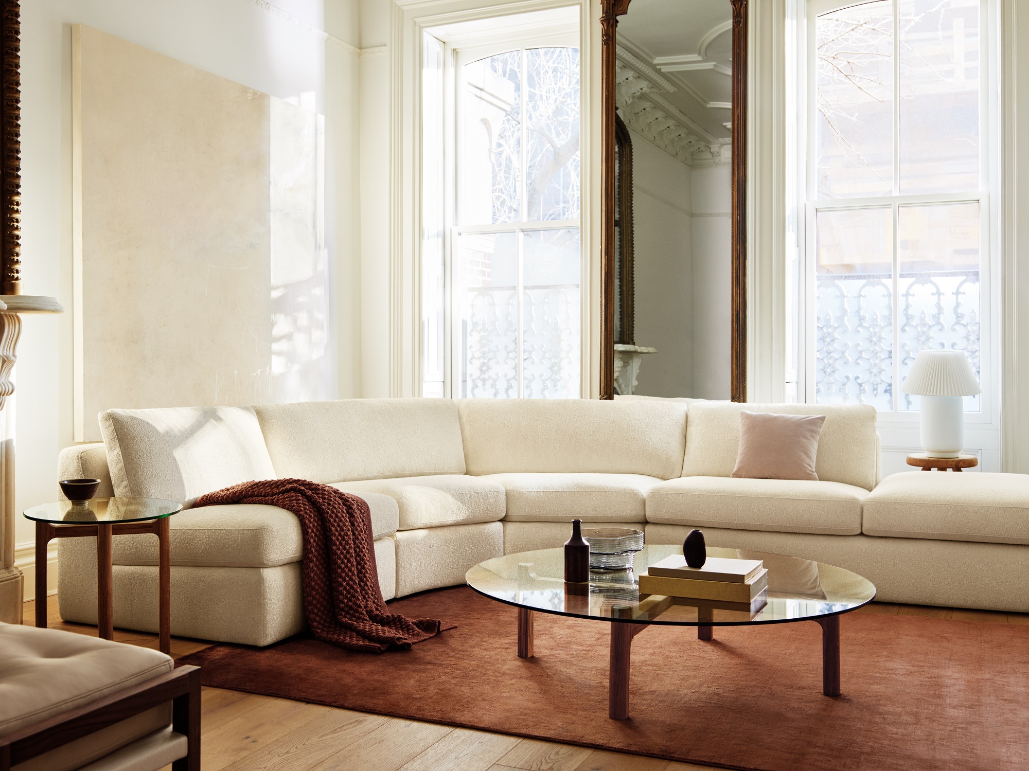 Glass top coffee table with walnut legs next to curved sofa in luxurious living space 