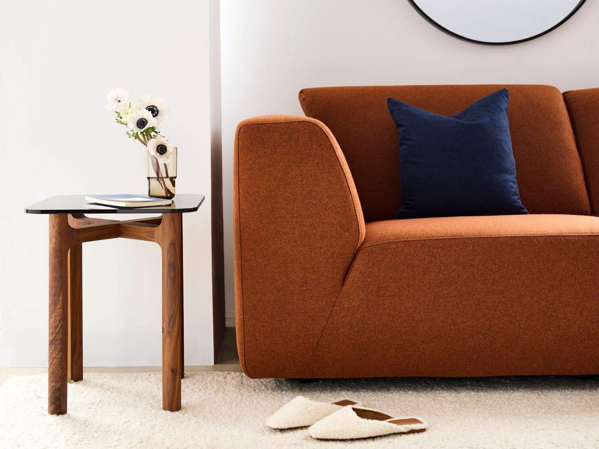 Brown glass tumbler with flowers in it on side table near orange sofa