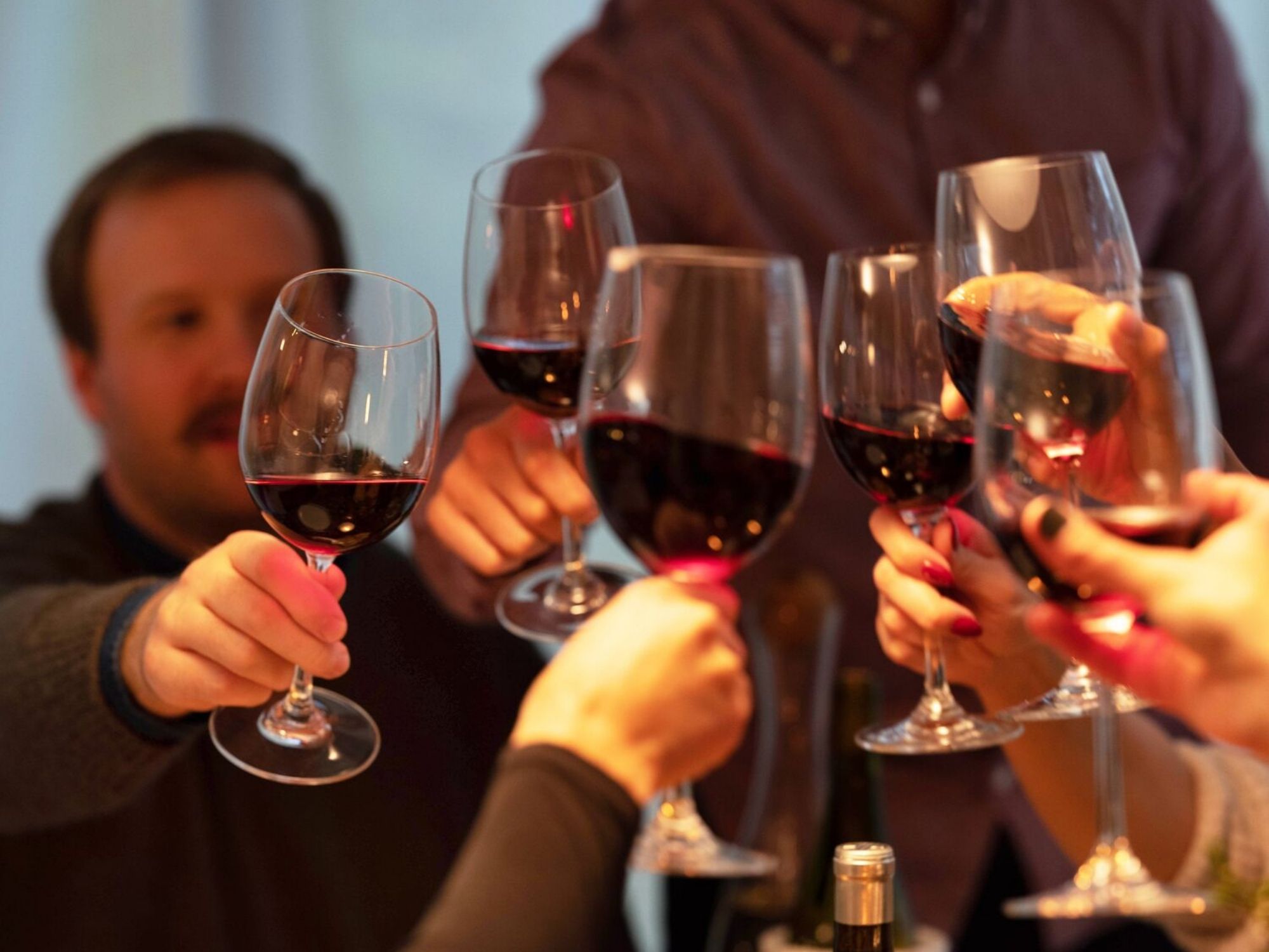 Dinner party guests toast with modern red wine glasses