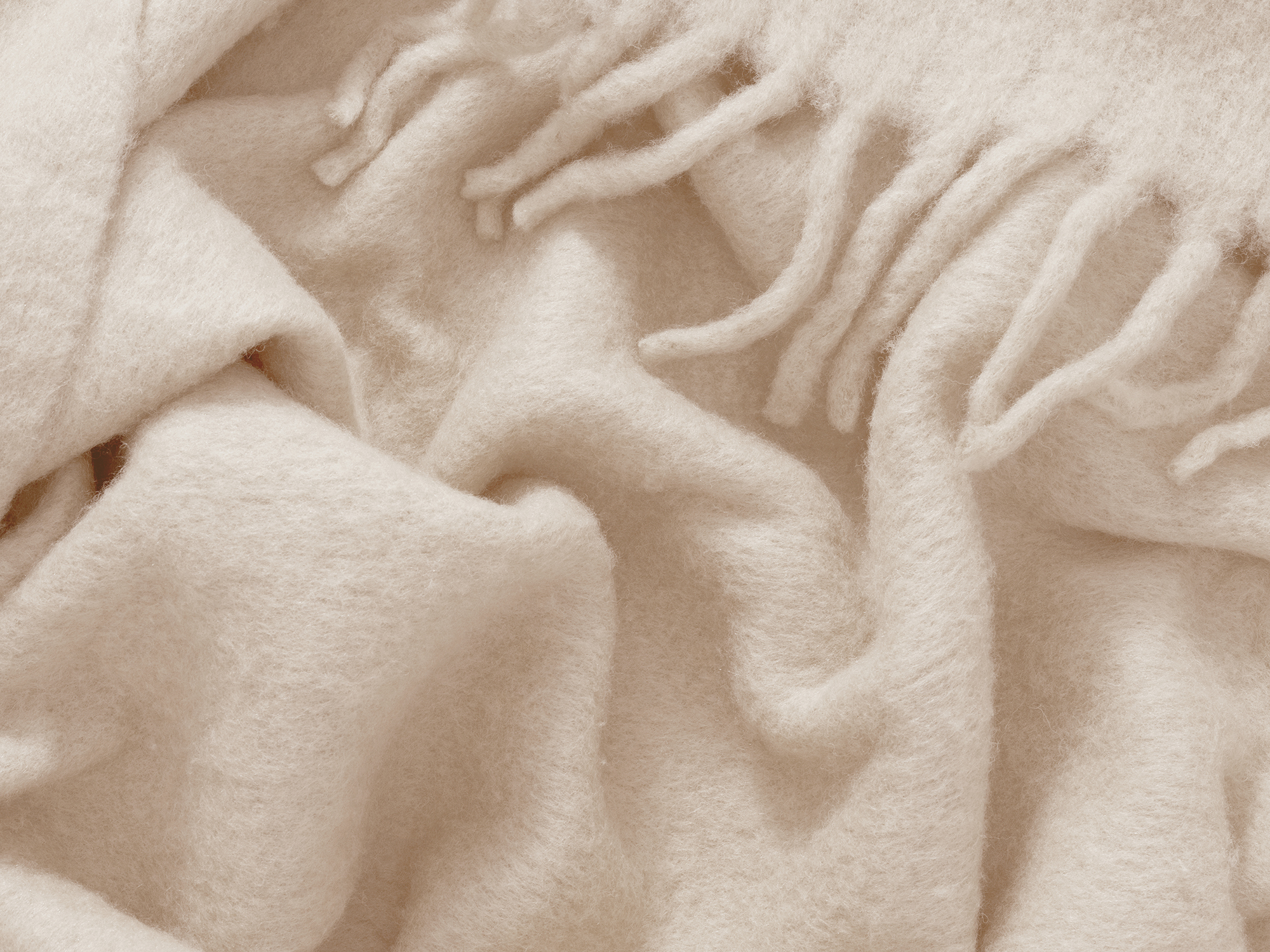 Detail view of wrinkled ivory wool throw with tassels