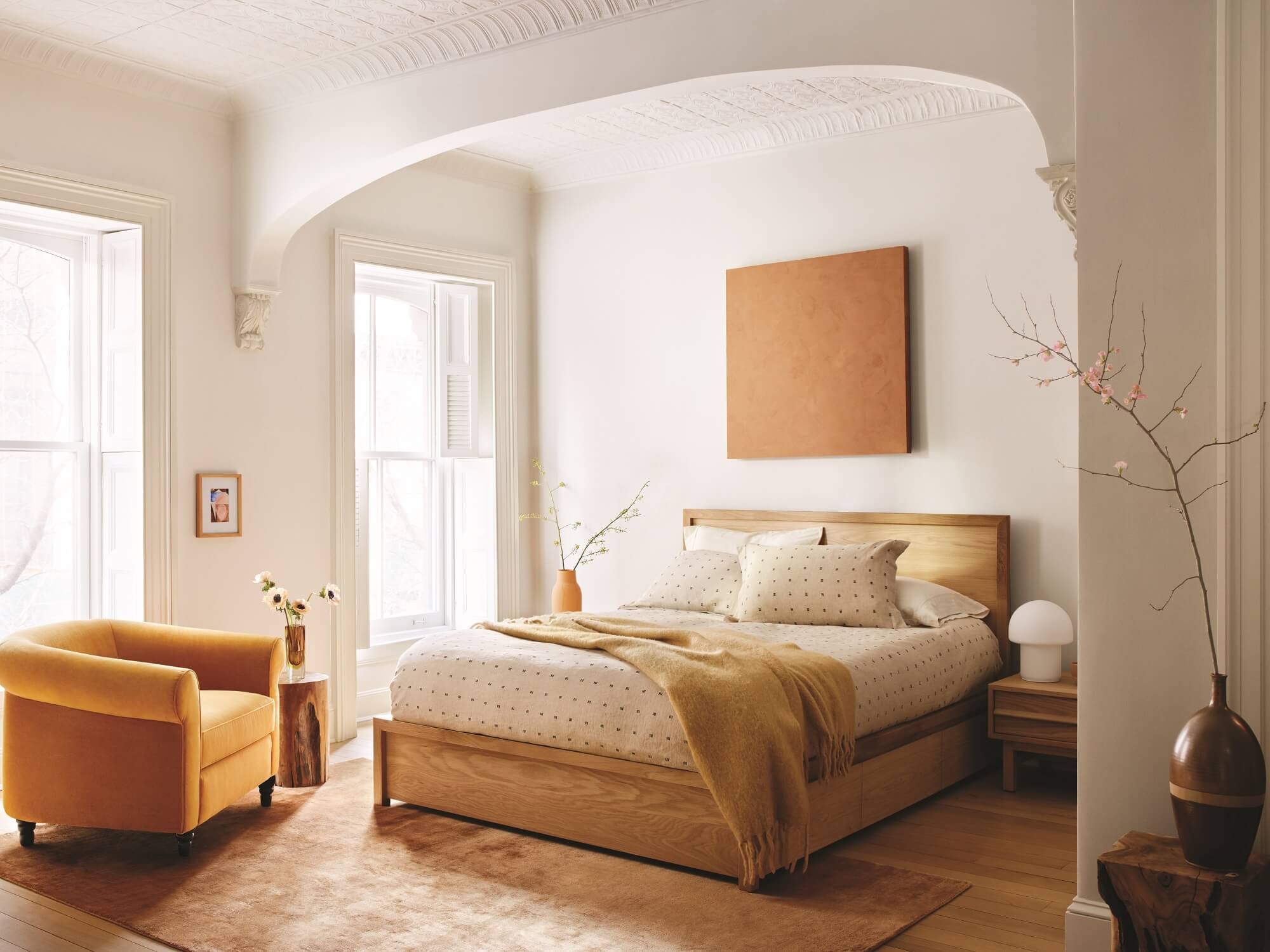 Oak storage bed beside orange armchair in neoclassical inspired modern bedroom 