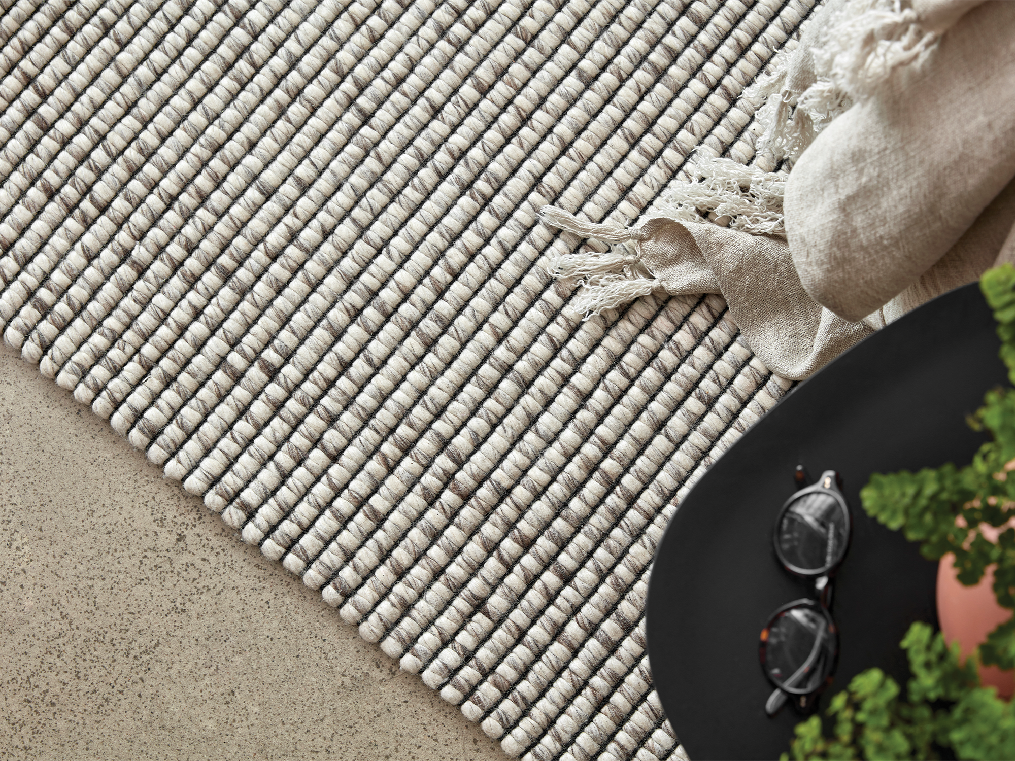 Grey and cream woven wool area rug with black side table and beige throw