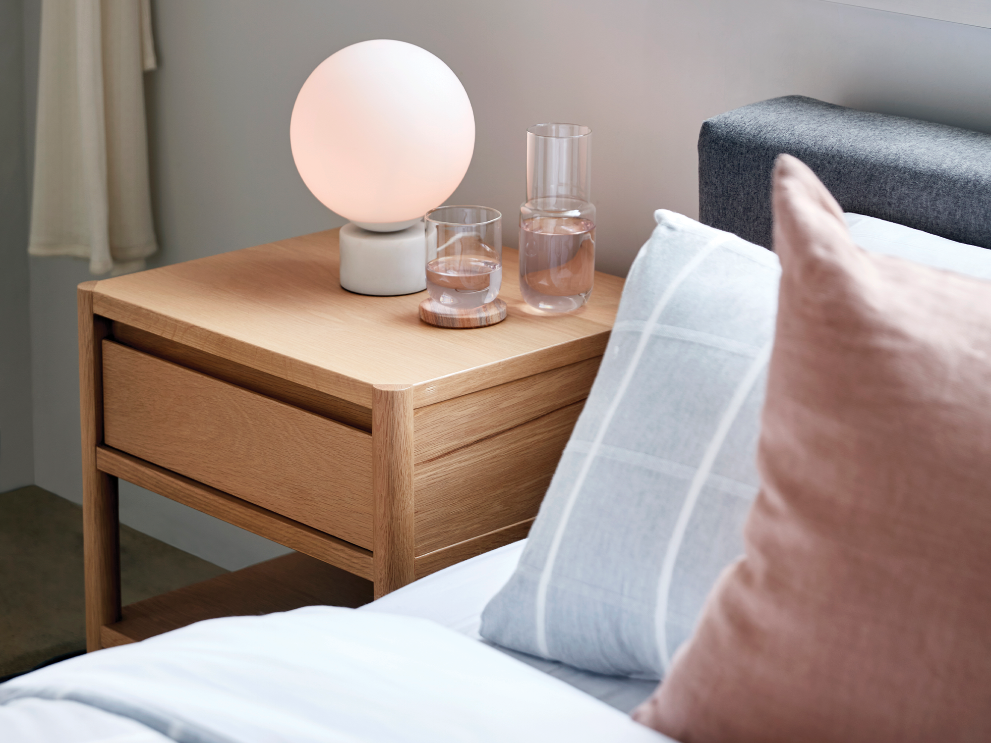 White marble table lamp and two water glasses on an oak nightstand