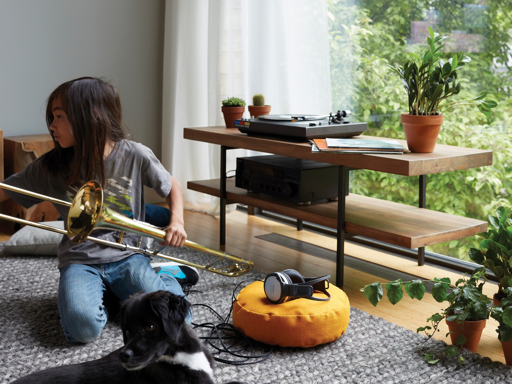 A little girl with a trombone sits beside the reclaimed teak modern media console with a record player on it