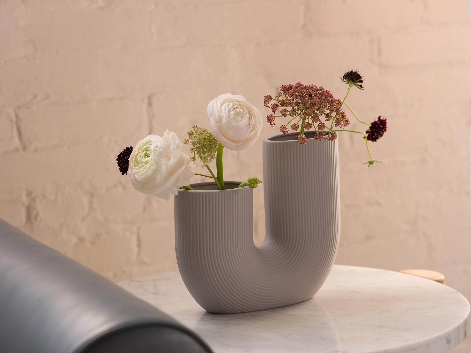 Grey curved decorative vase filled with flowers on marble side table