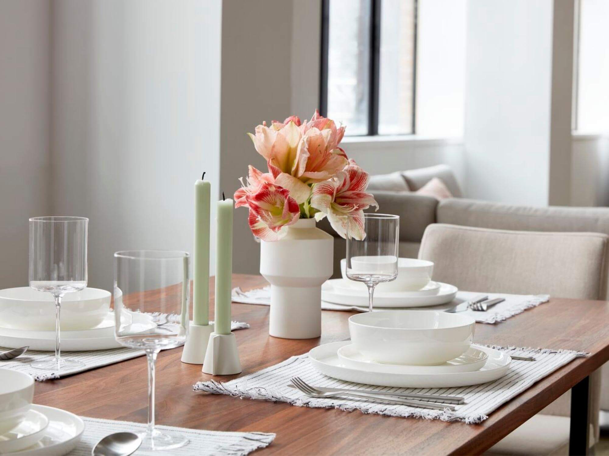 Two white angled candleholders on dining table set for four