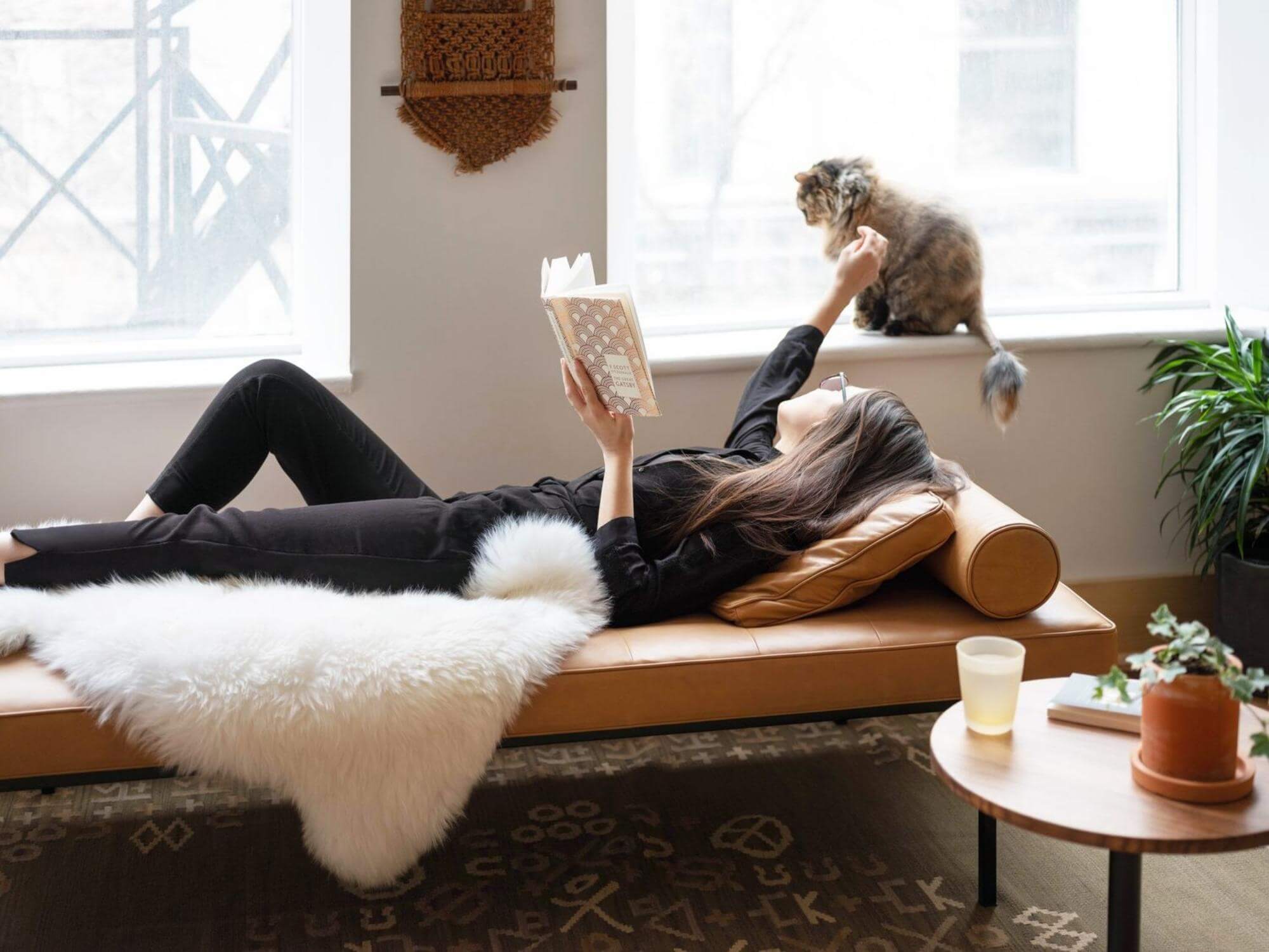 Woman lying on a brown leather chaise with sheepskin rug on it