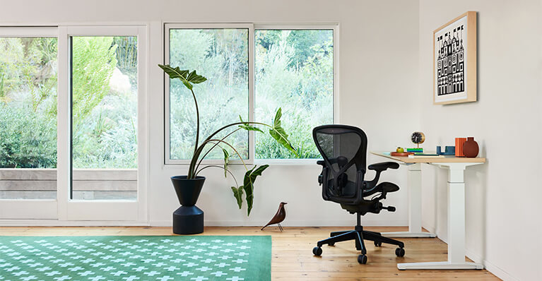 black herman miller aeron office chair is shown in front of oak desk in a home office setting. Link to herman miller sale page