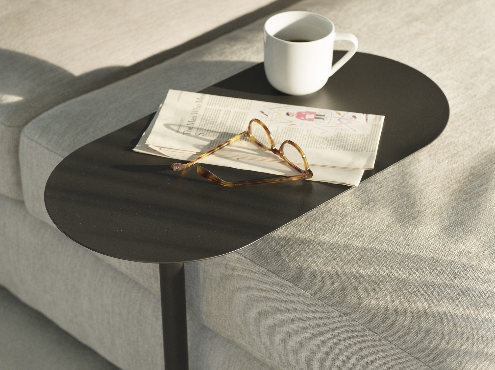 The Finn side table in black with a pair of glasses, newspaper, and cup of coffee on it floats above a beige sofa