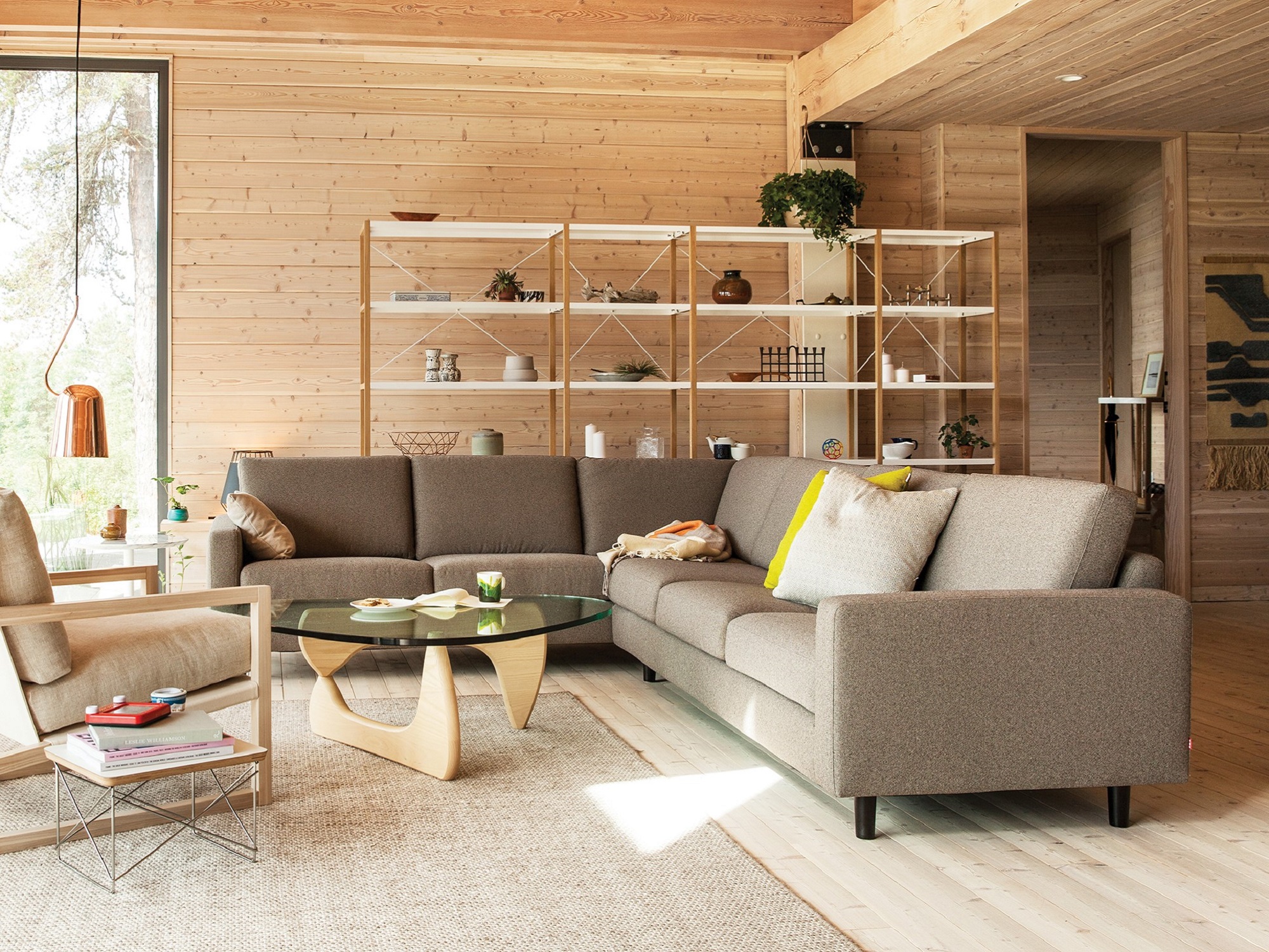 The Oskar l shape sofa in light grey fabric in a wood paneled living room with the Noguchi coffee table and Chiara chair