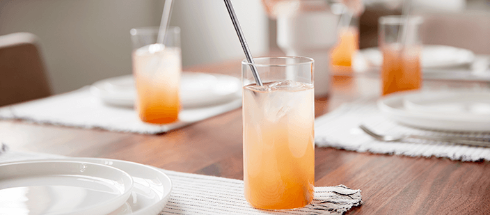 Juice and straws in water glasses with placemats and dishes on walnut table