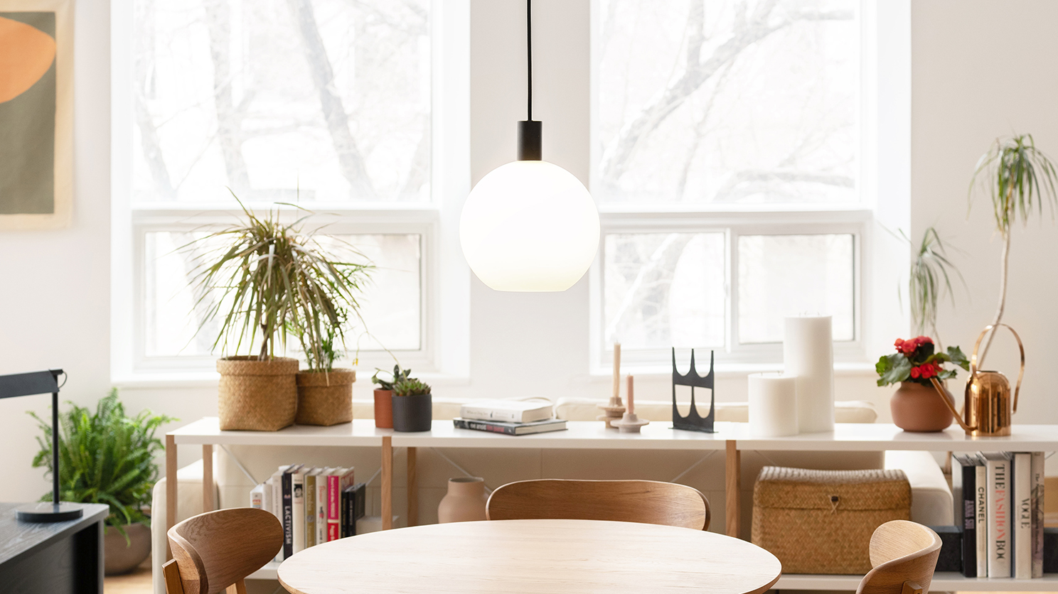 The Wellington Glass Shade pendant light hangs over a dinette table with a shelving unit stacked with books in the background