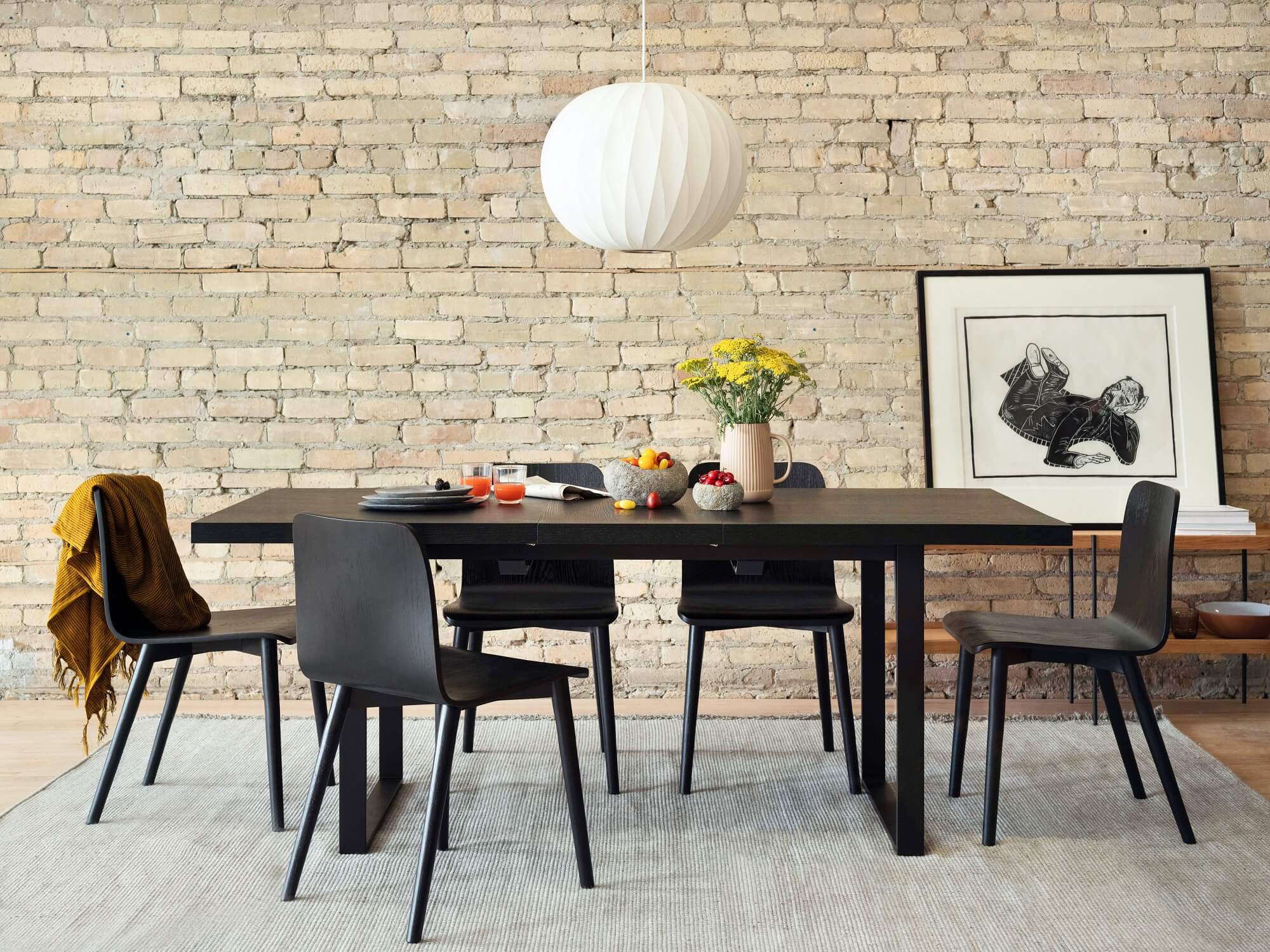 Black wood dining chairs around an expandable dining table in exposed brick room