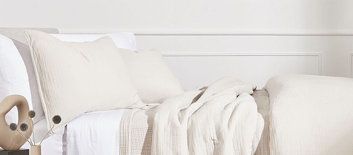 White and ivory bedding on bed against white wall