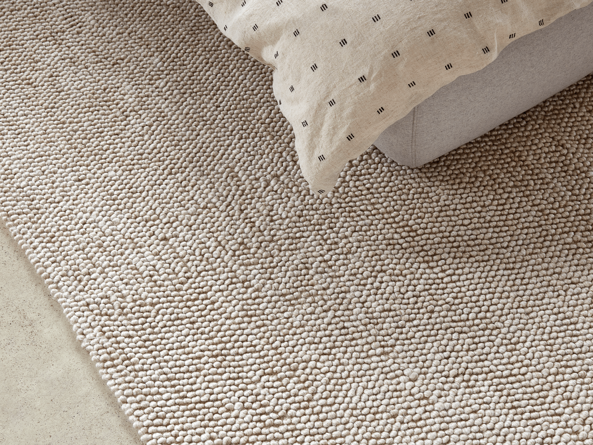 Beige wool rug under a grey upholstered bed with beige duvet set