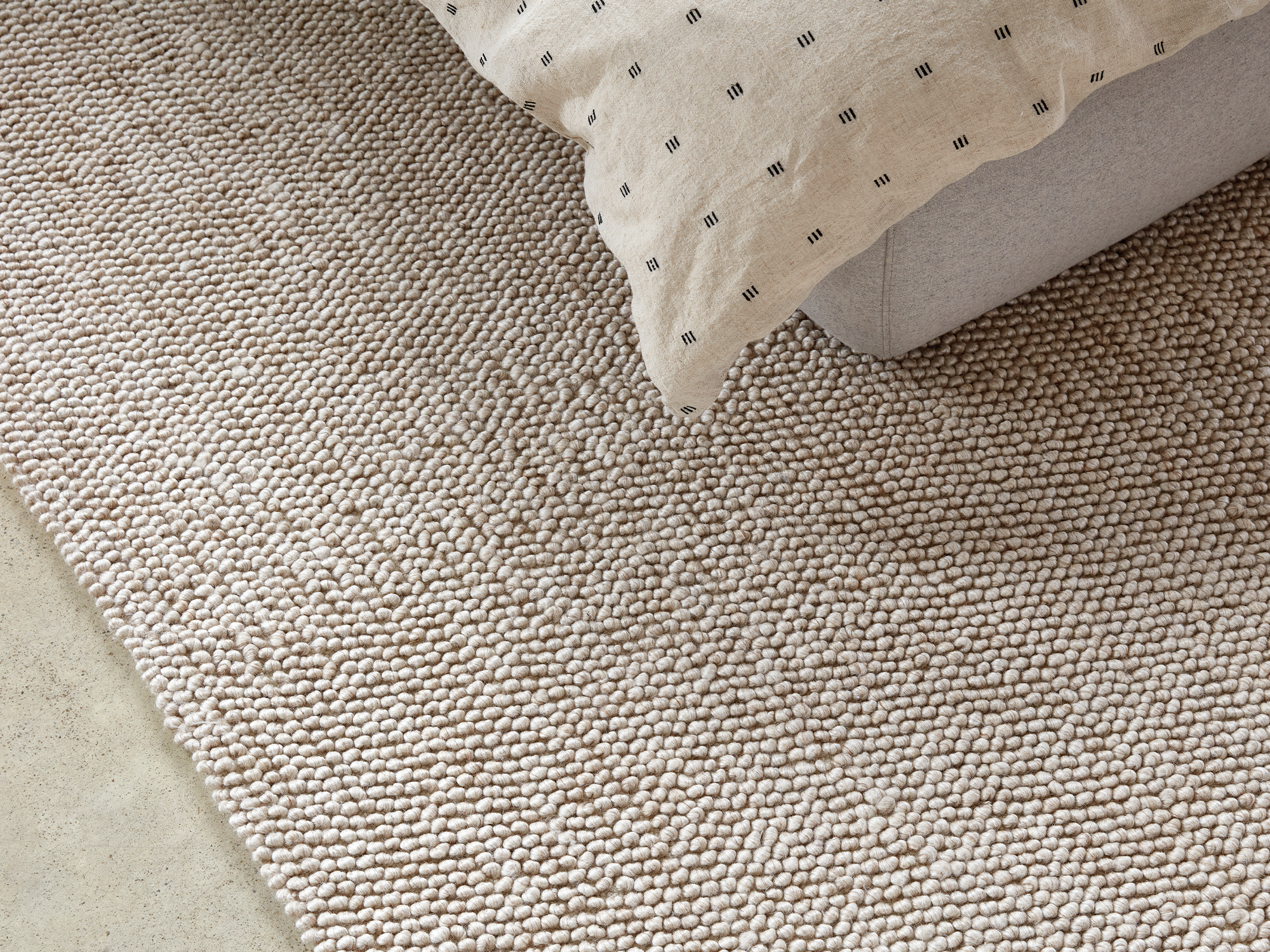 Beige wool rug under a grey upholstered bed with beige duvet set