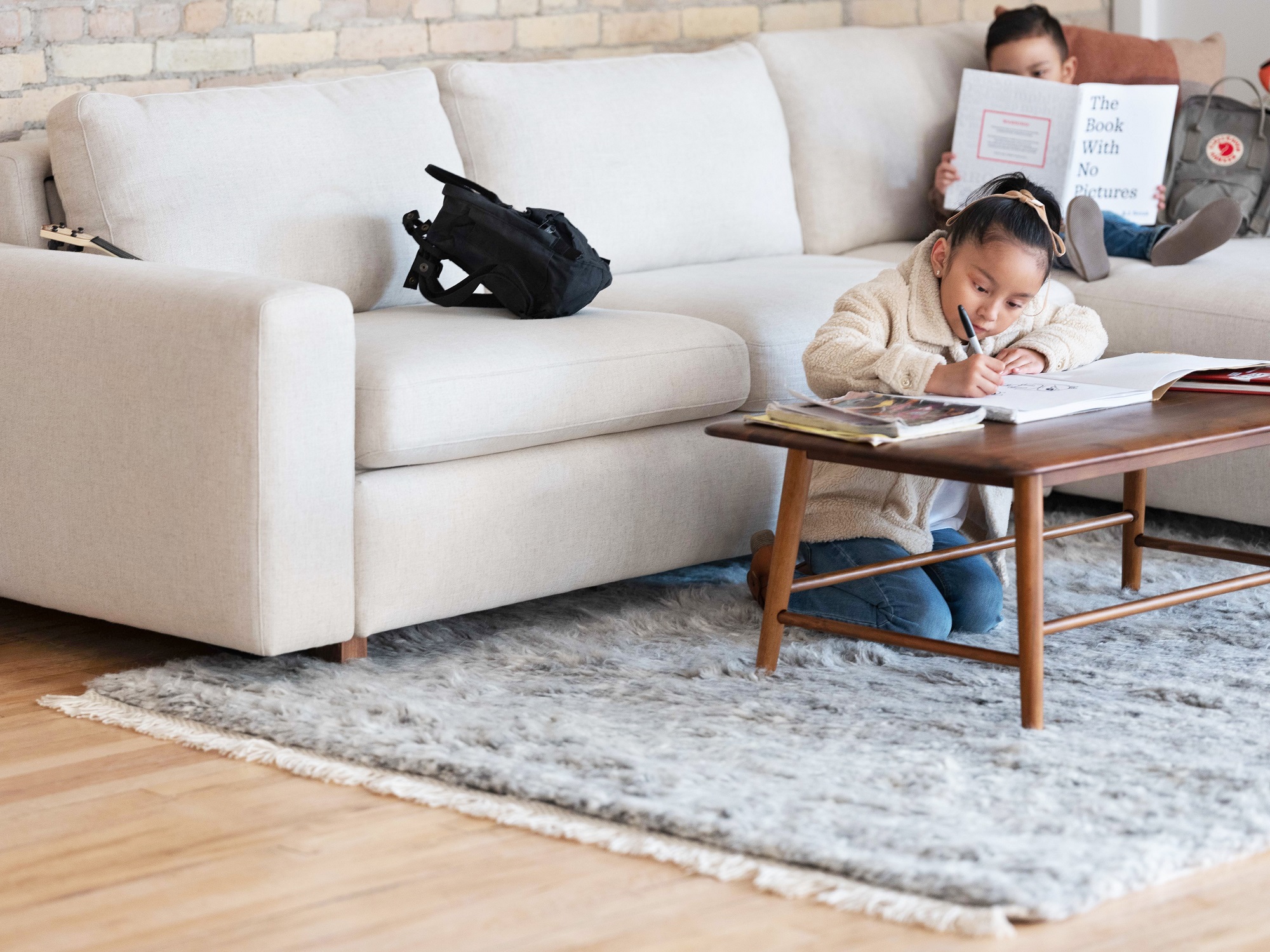 A little girl kneels at the Kacia solid wood coffee table in java and colours in a colouring book