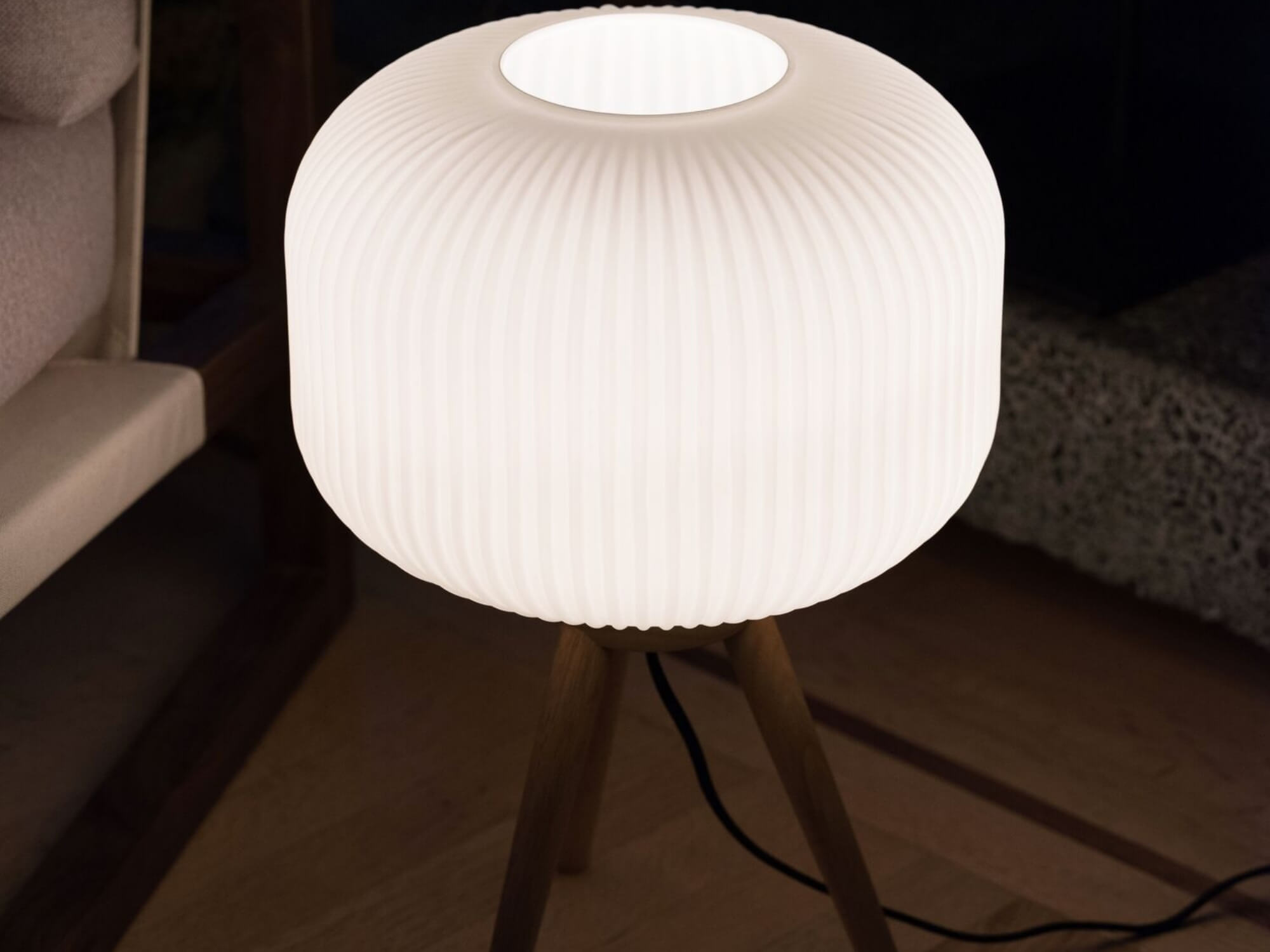 Lamp with oak legs and white shade on floor of dark room