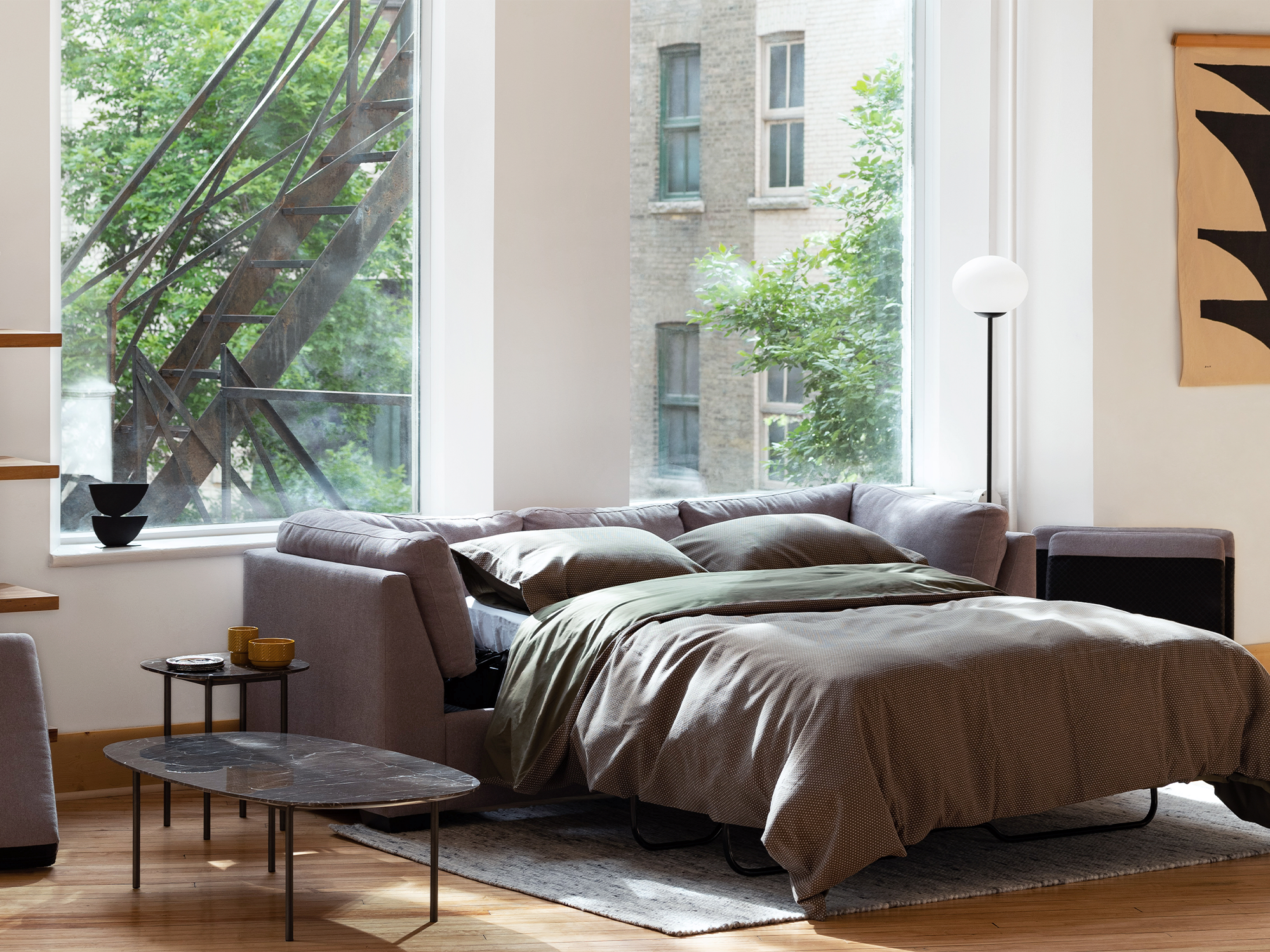 Grey sleeper sofa with bed open and grey bedding in a modern living space