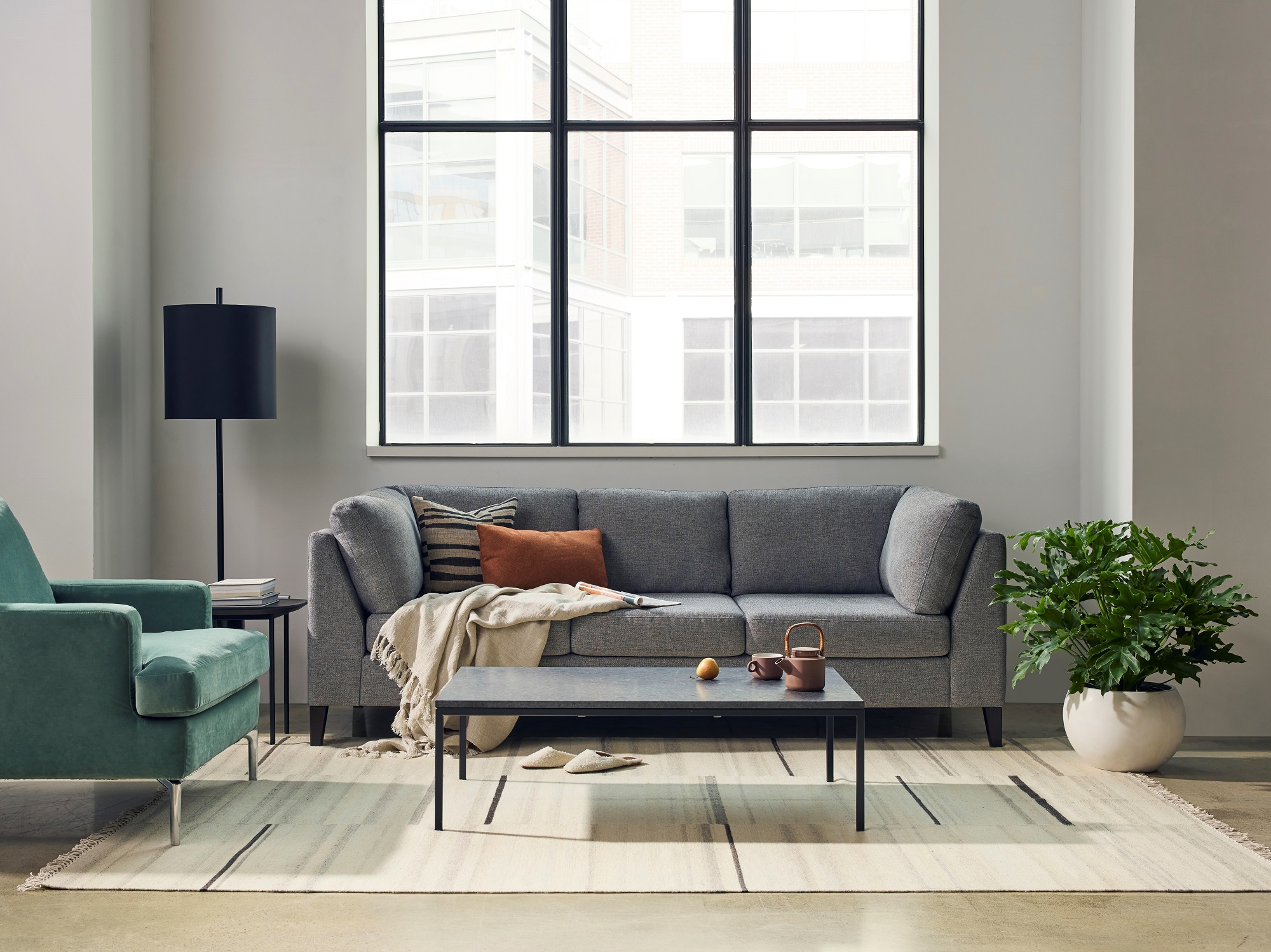 Green accent chair, grey sofa, and black coffee table sit on a beige rug