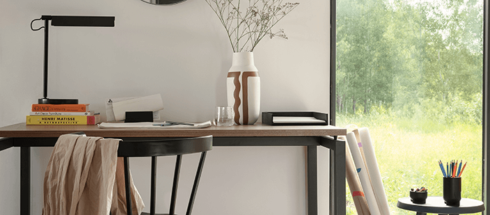 Walnut and black desk stacked with books beside black chair in modern home office