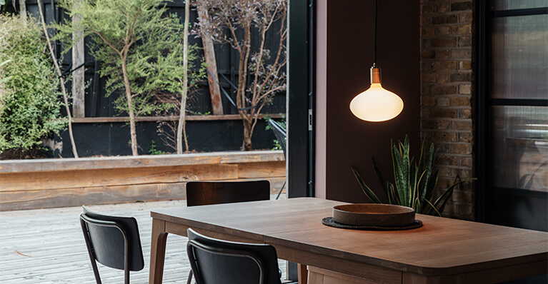 Large porcelain light bulb is displayed in a modern day rustic dining room. Link to Tala bulb category