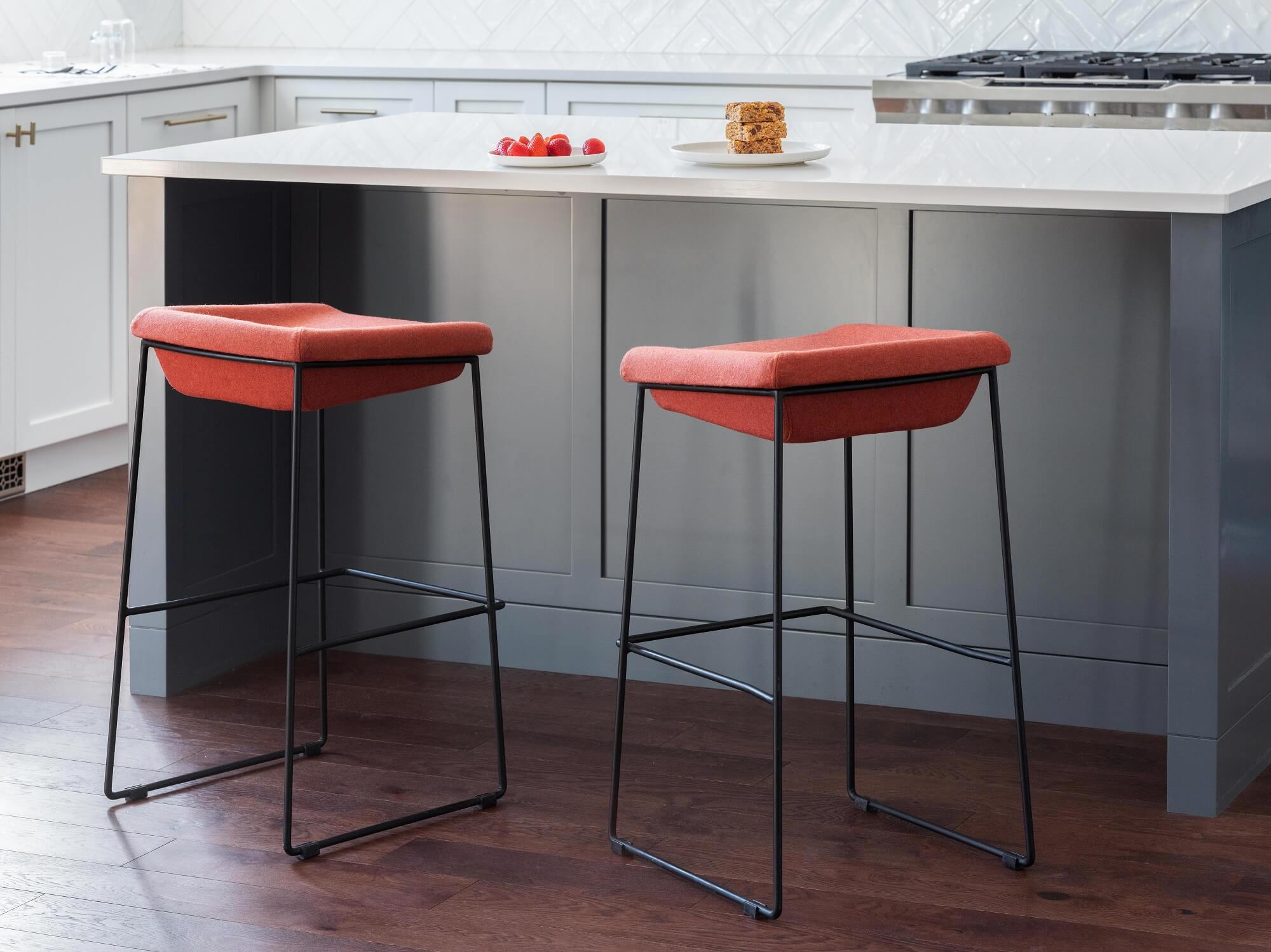 Counter height stools with red upholstered seat and black base sit at a kitchen island