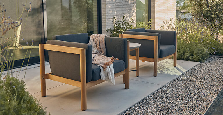 Two grey fabric outdoor chairs are displayed on a cement patio. Link to neighbor brand category