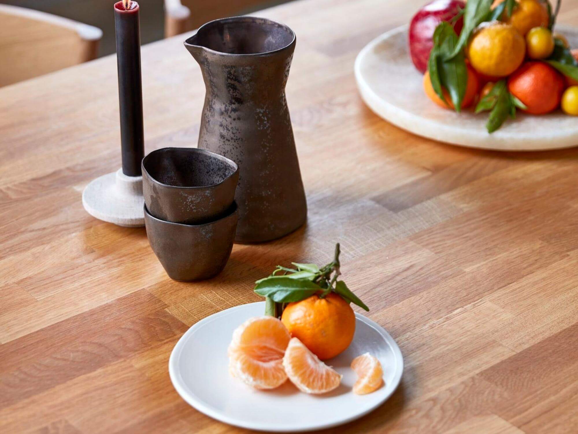 Stone plate on dining table with candle, cups, and metal jug